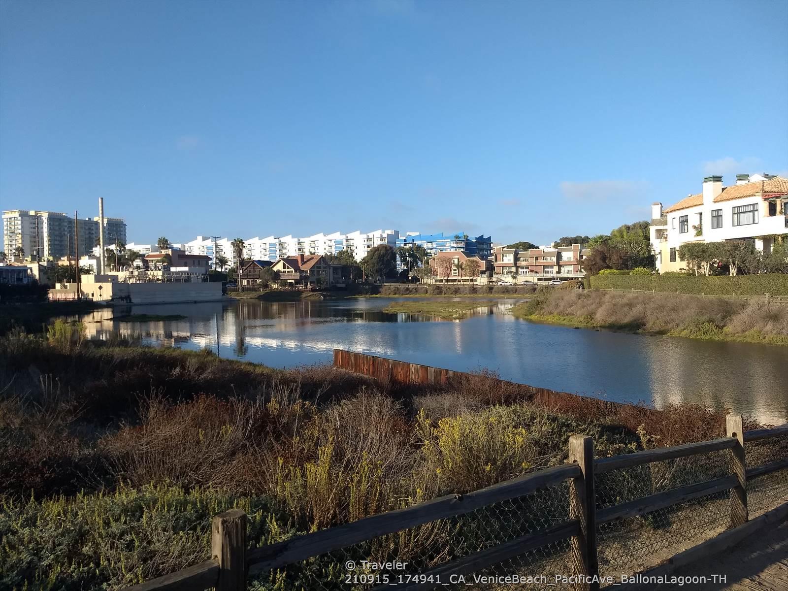 Sunny view of a calm lagoon surrounded by buildings and lush vegetation.