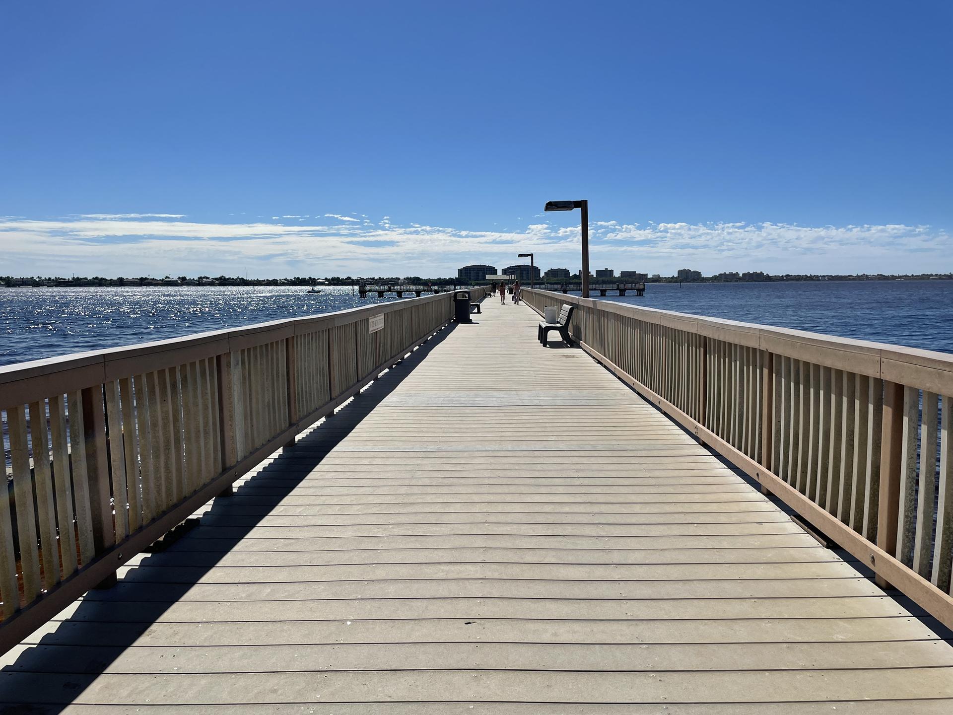 A long wooden pier extends over a wide body of water on a sunny day.