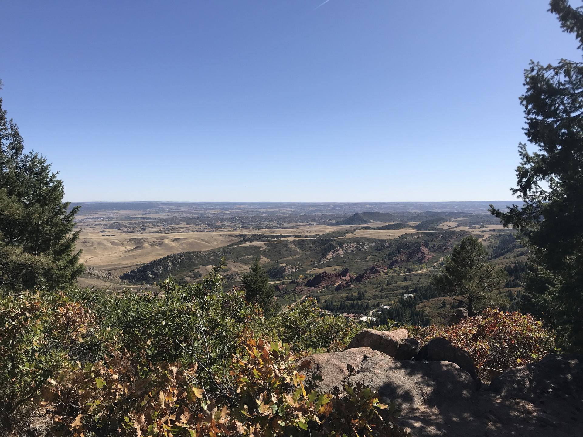 Panoramic view of a wide valley and distant plains under a clear blue sky.