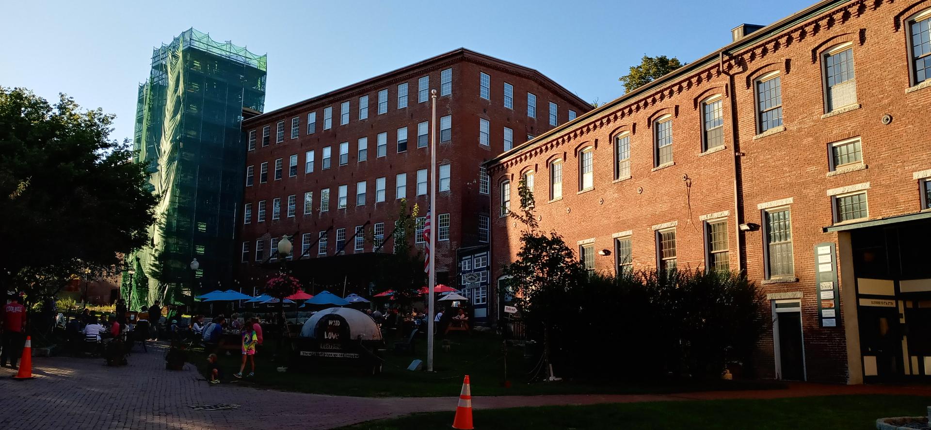 Large brick buildings with outdoor seating area in warm, late afternoon light.