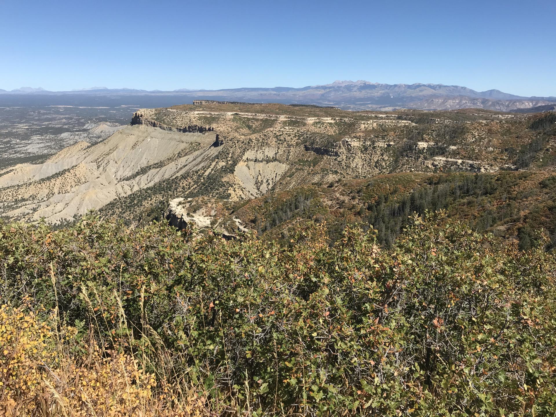 Rugged canyon landscape with distant mountains and a clear blue sky.