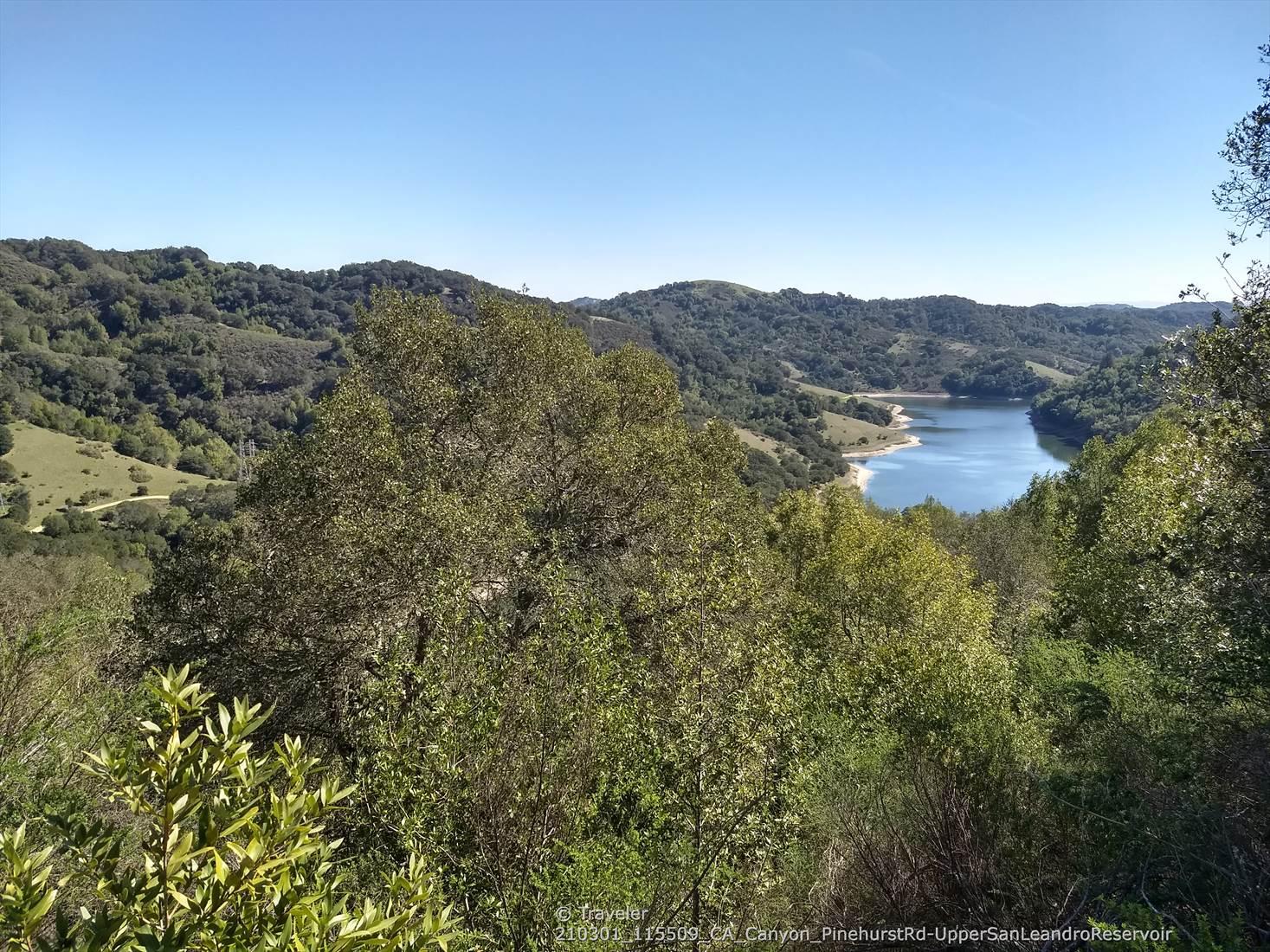 Panoramic view of a blue lake nestled among lush green, tree-covered hills.