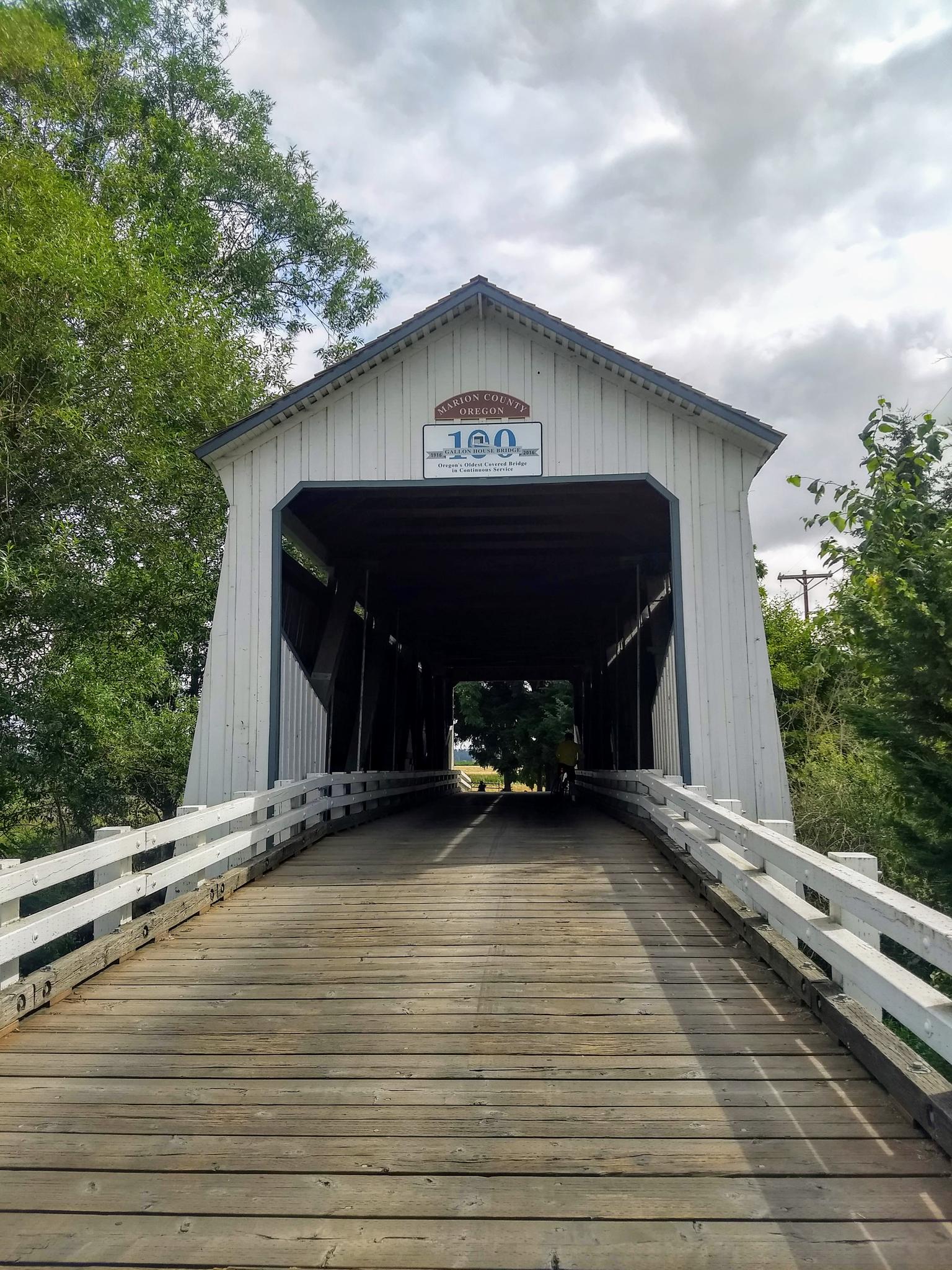 Wooden covered bridge with white railings under a cloudy sky.