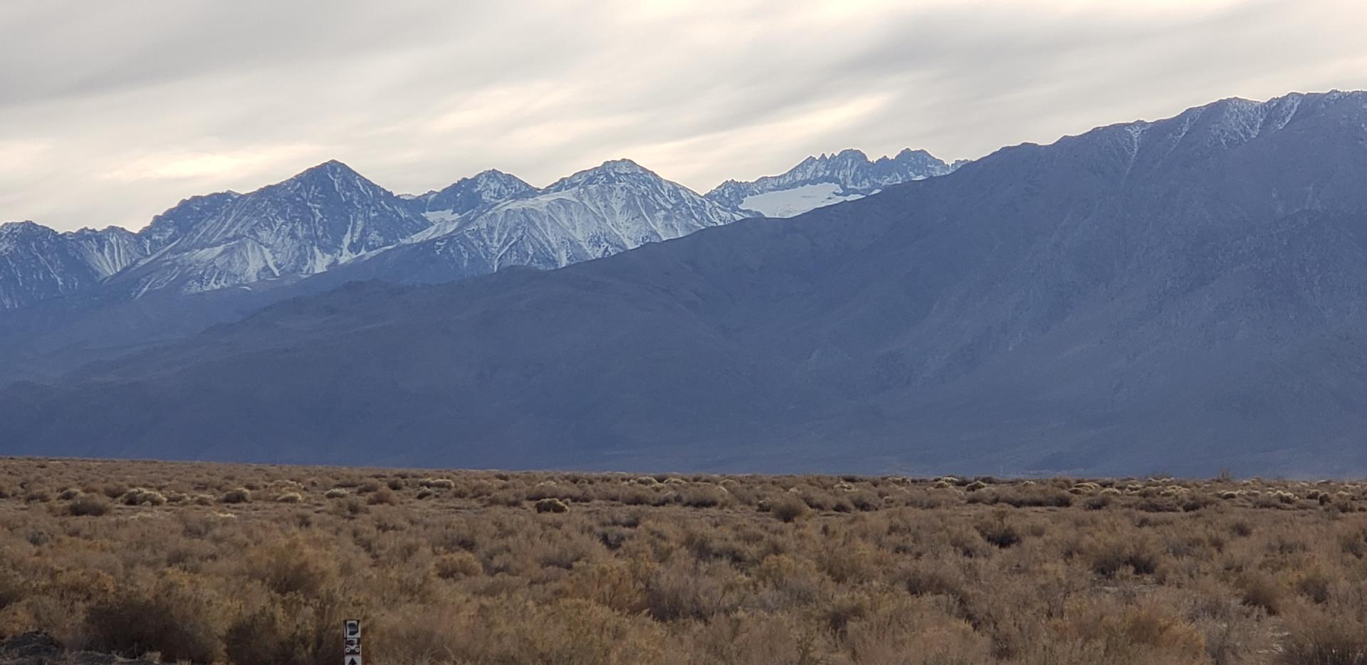 Vast desert scrubland with snow-capped mountains under an overcast sky.