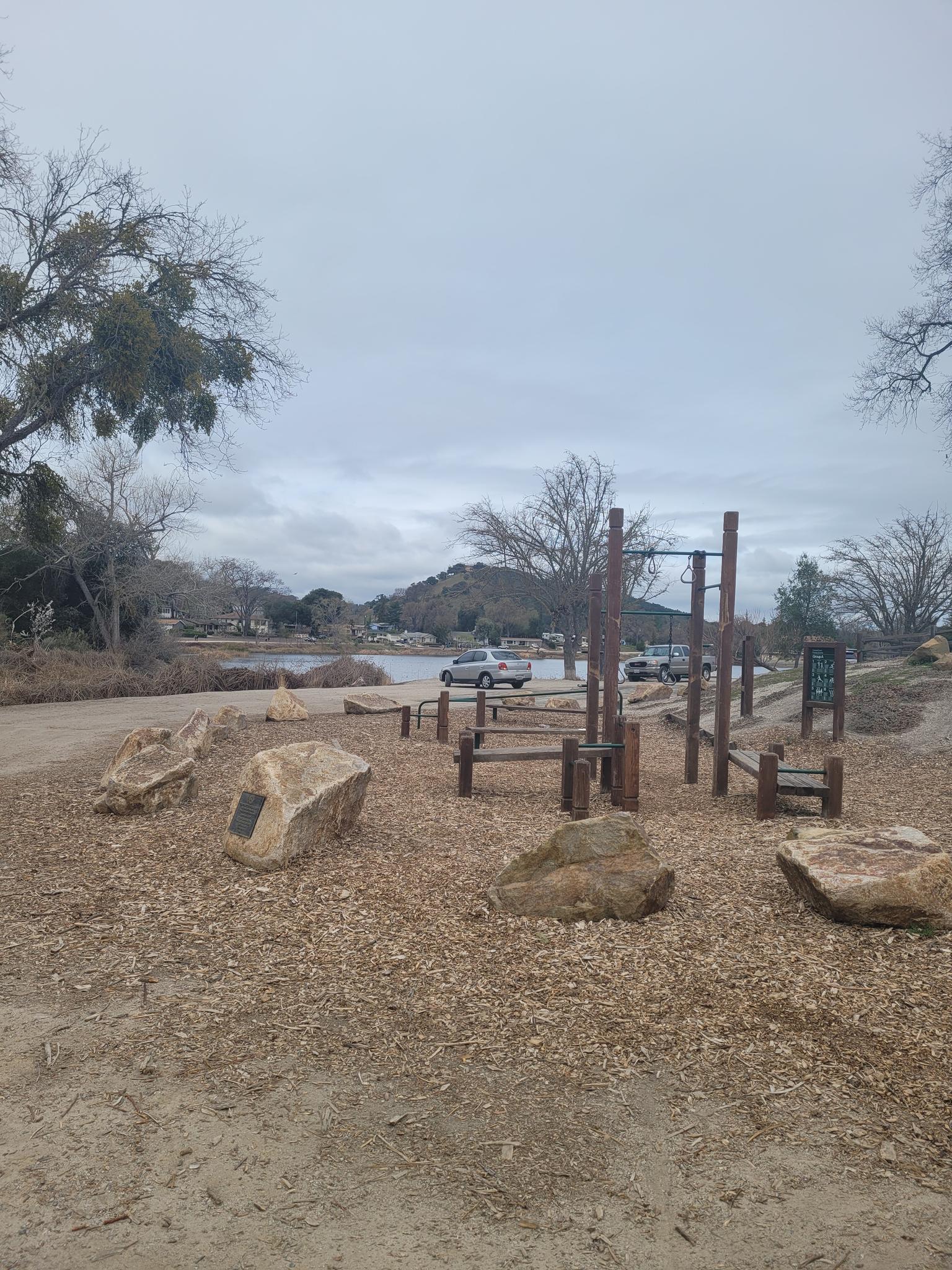 Outdoor exercise area with wooden equipment and rocks under an overcast sky.