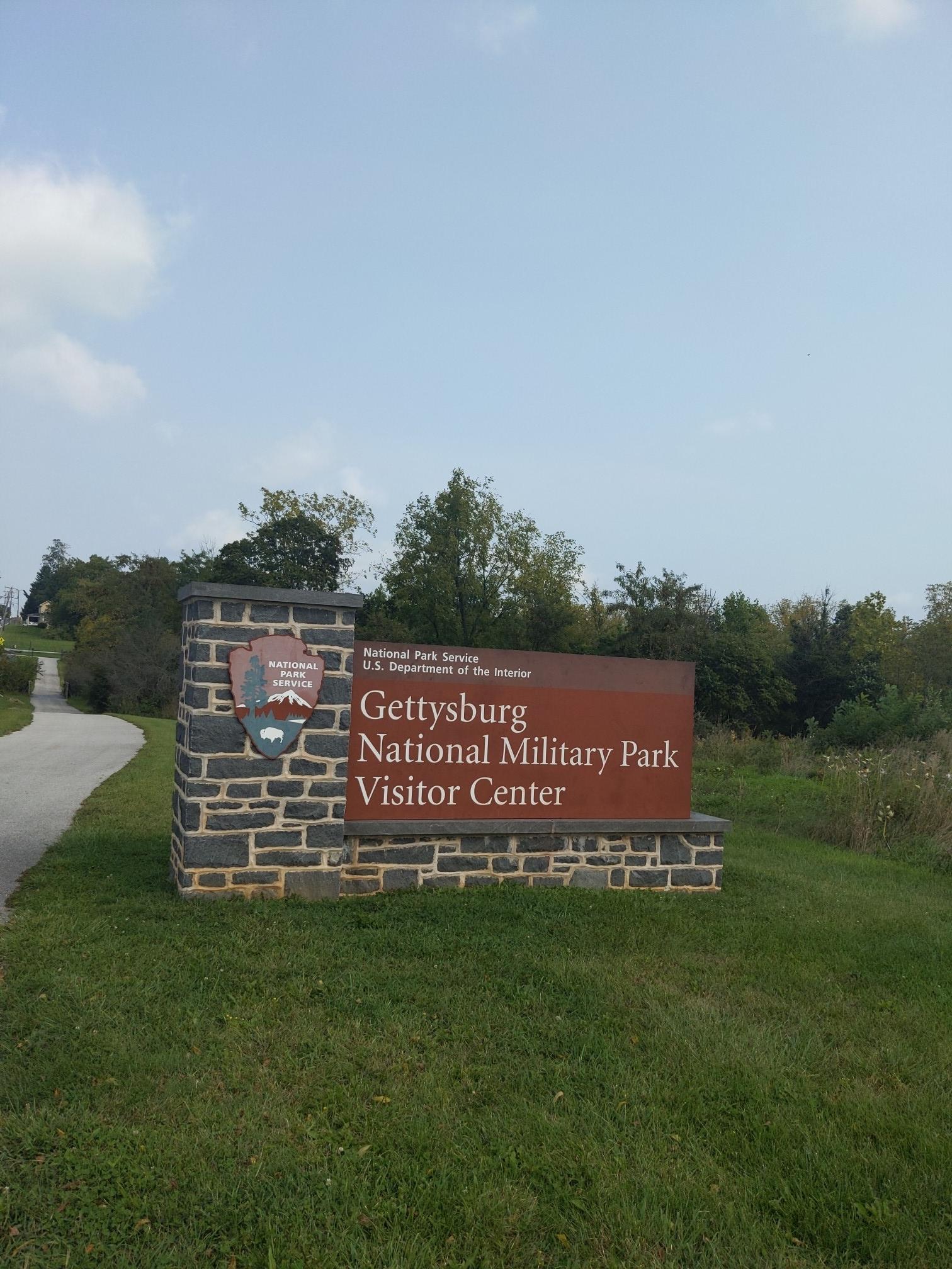 A stone and brown sign for a visitor center on a grassy hill.