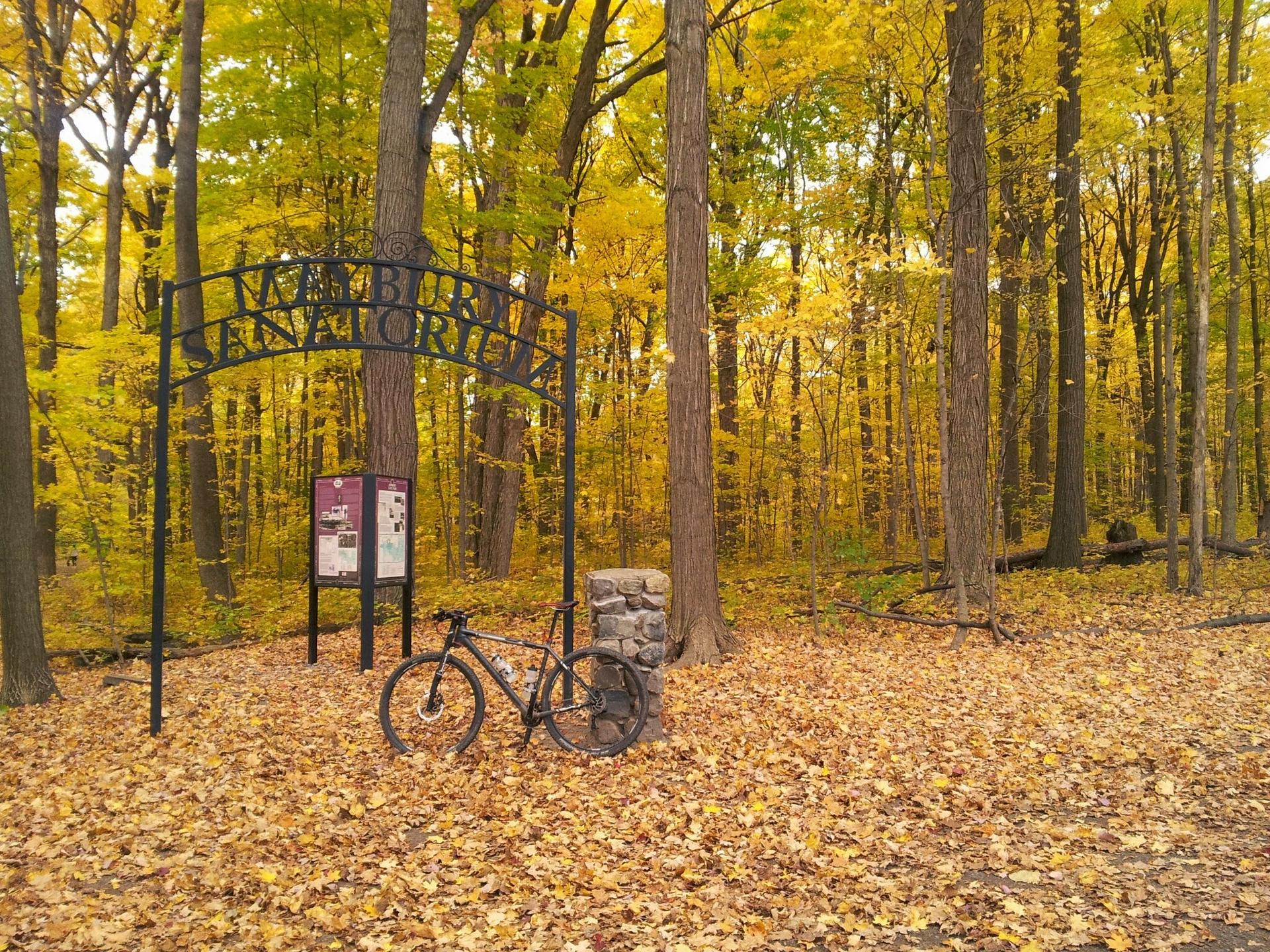 A bicycle rests by an archway sign in a vibrant autumn forest.