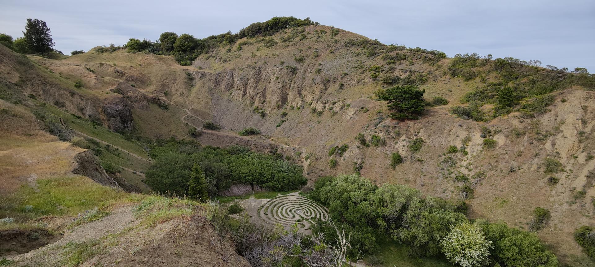 A large, rocky canyon features a labyrinth pattern on its green floor.
