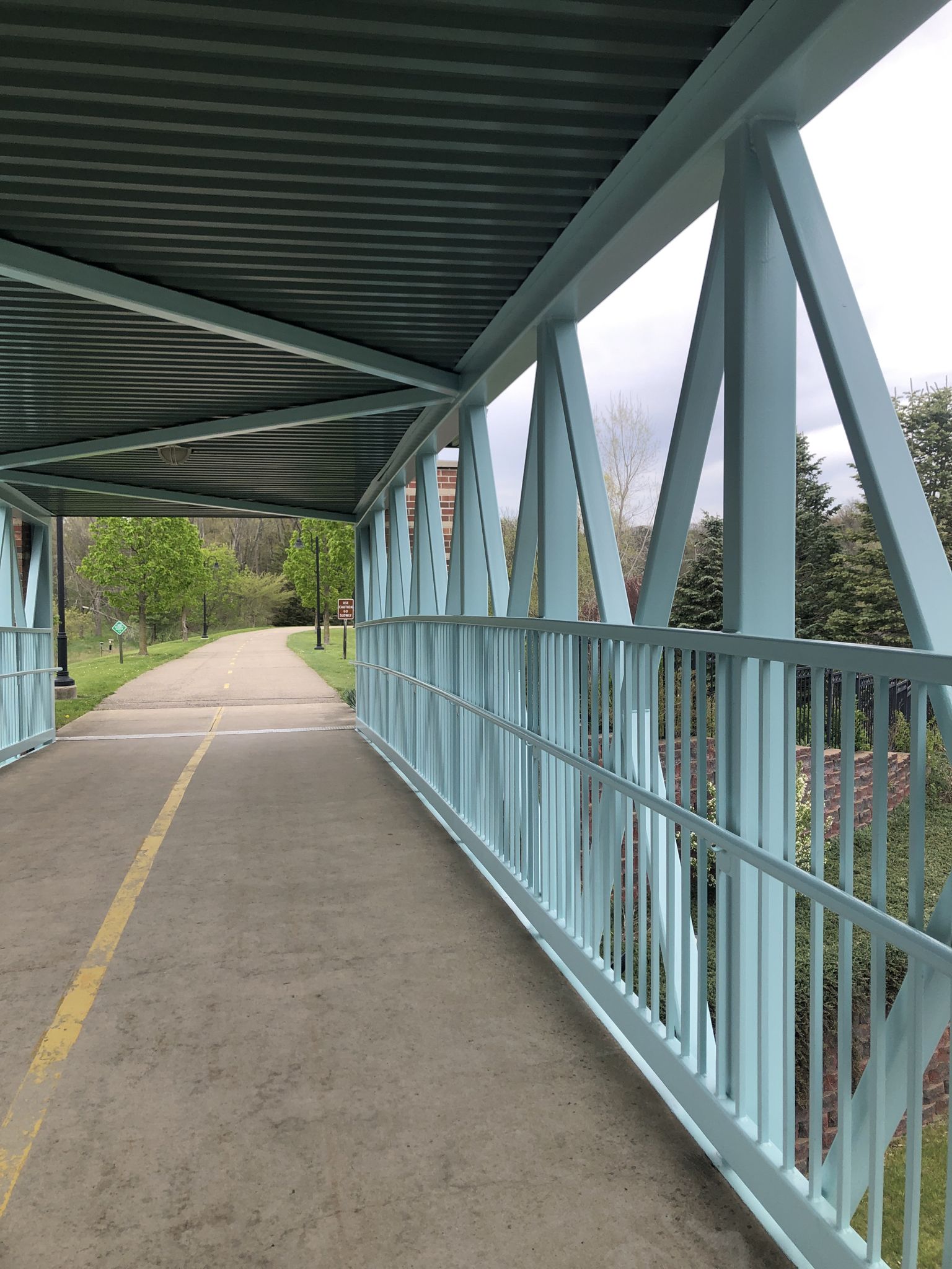 Covered pedestrian bridge with light blue railings, concrete path, and green trees. - Milham Road Bridge loop from Westfield Park