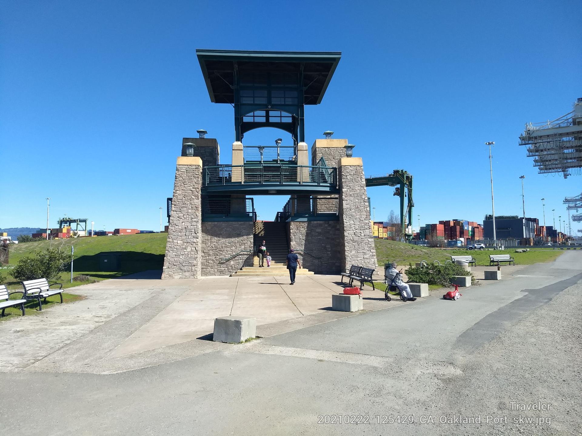 Stone observation tower on a sunny day with people and distant cranes.