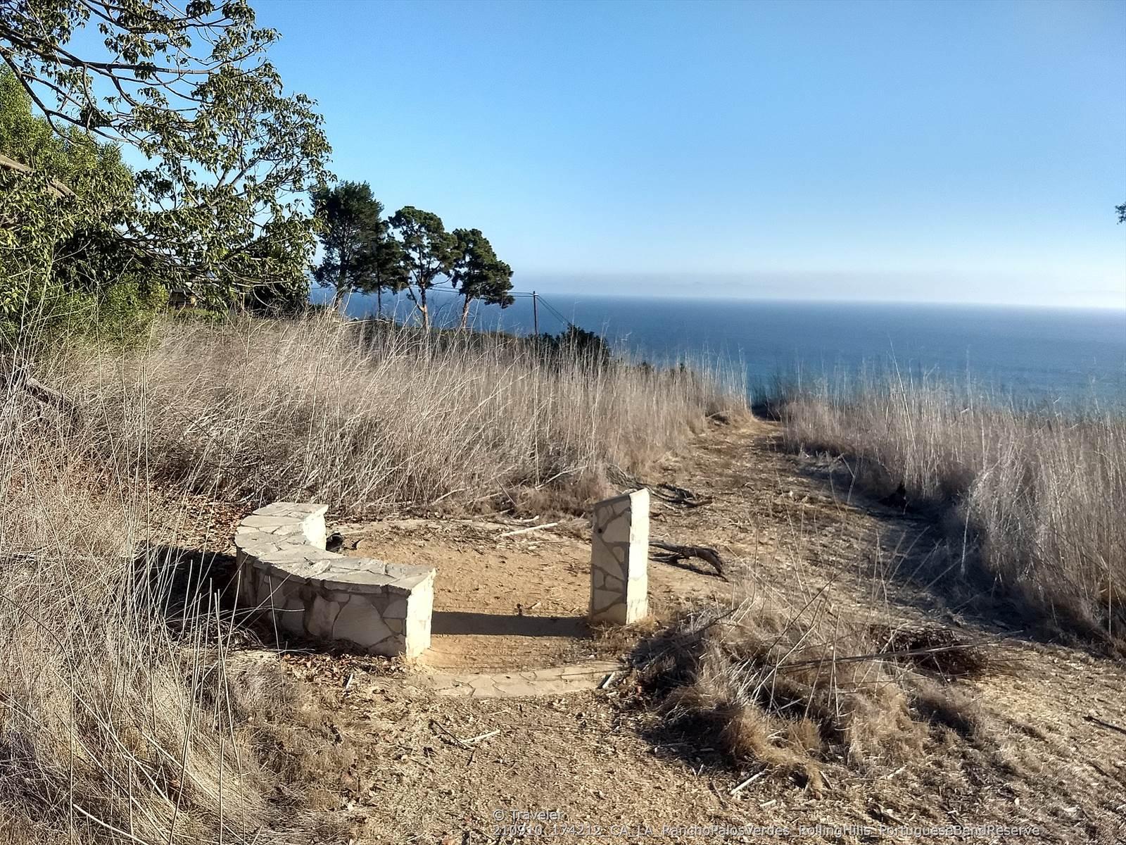 Stone bench and monument on a hill overlooking the ocean and dry grass.