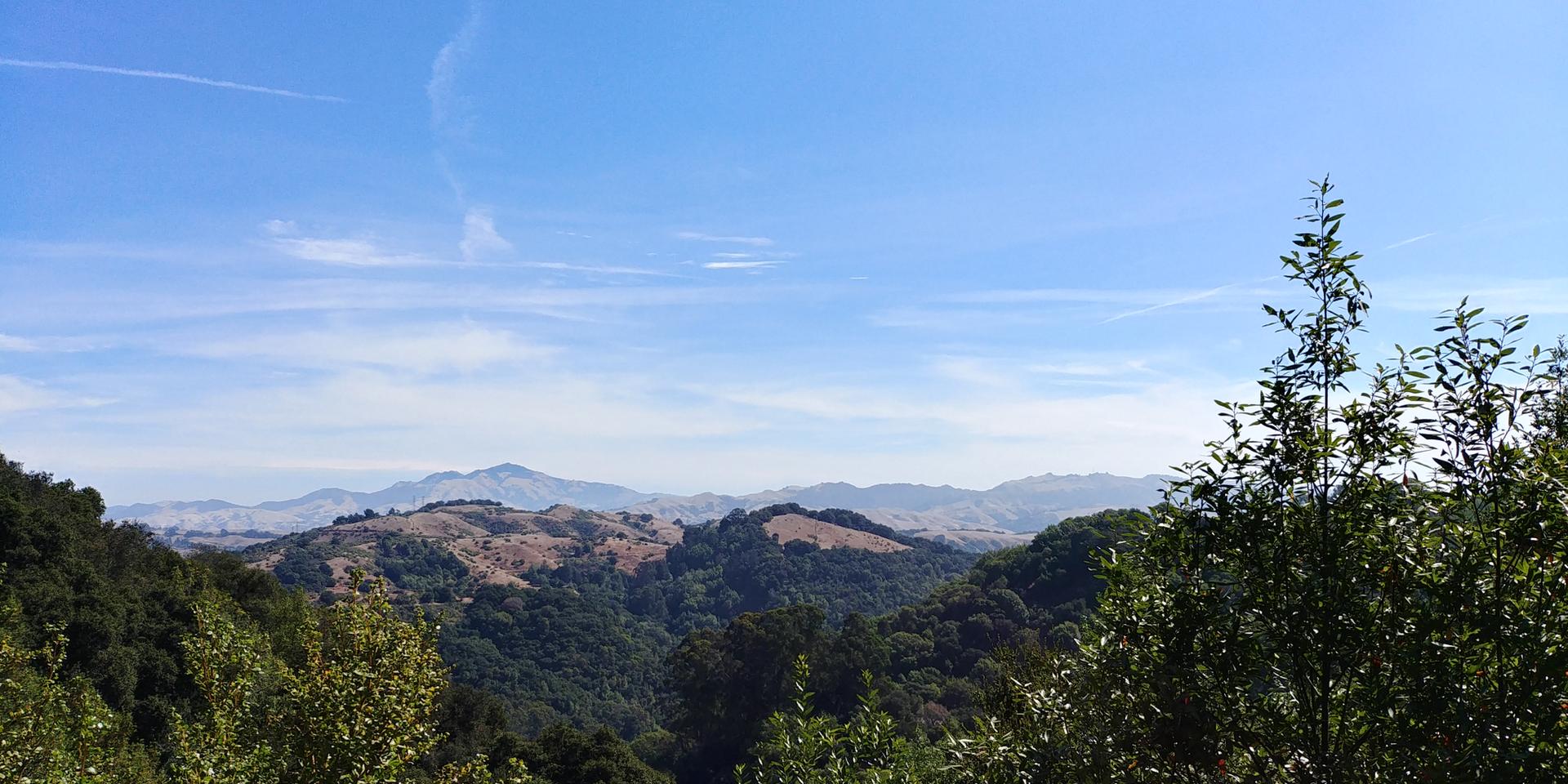 Expansive view of green rolling hills and distant mountains under a bright blue sky.