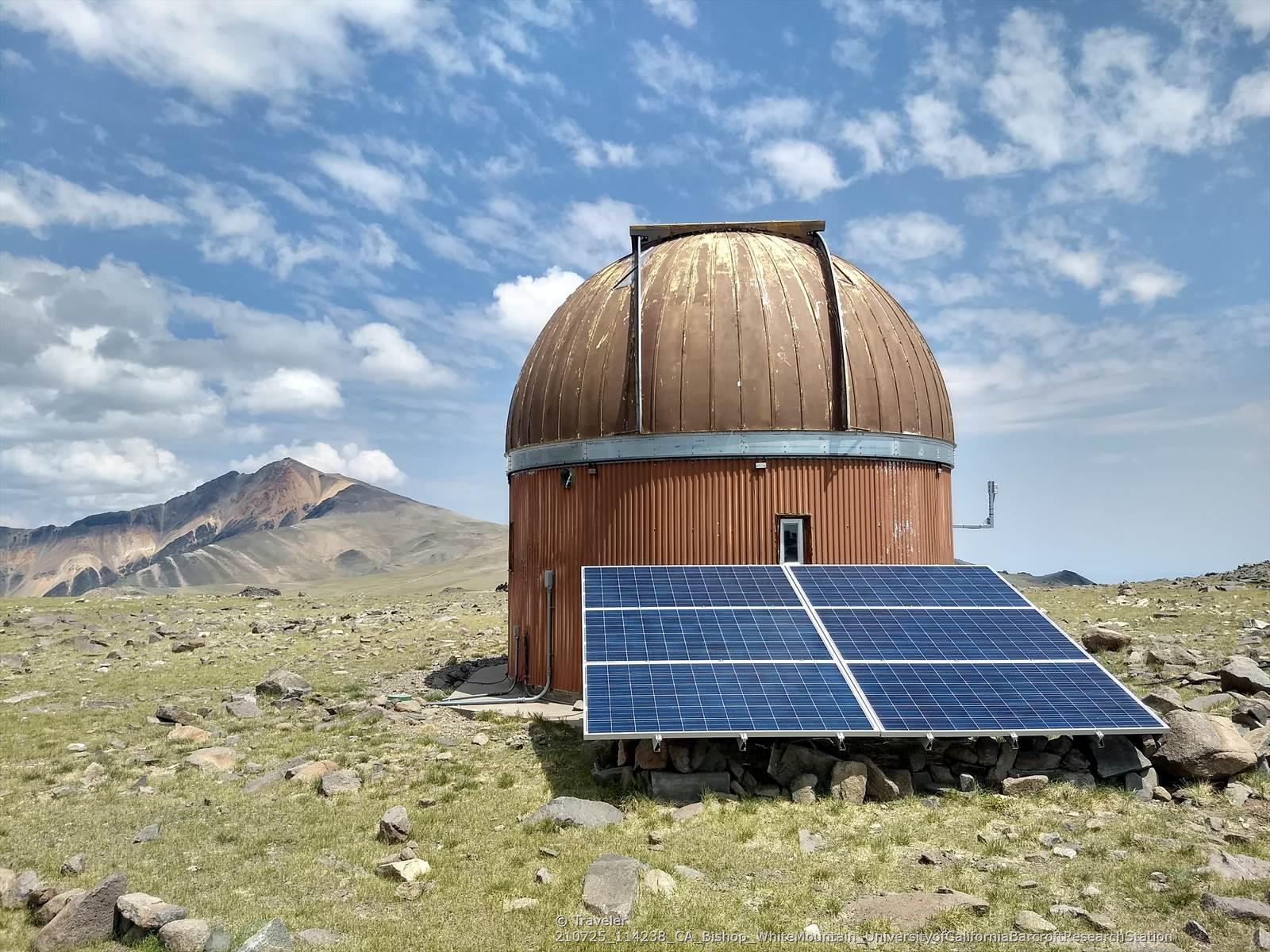 Observatory dome and solar panels on a grassy, rocky plain.