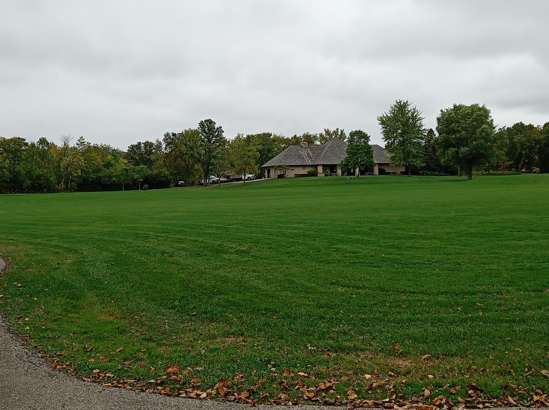 A vast green lawn with a house and trees under an overcast sky.