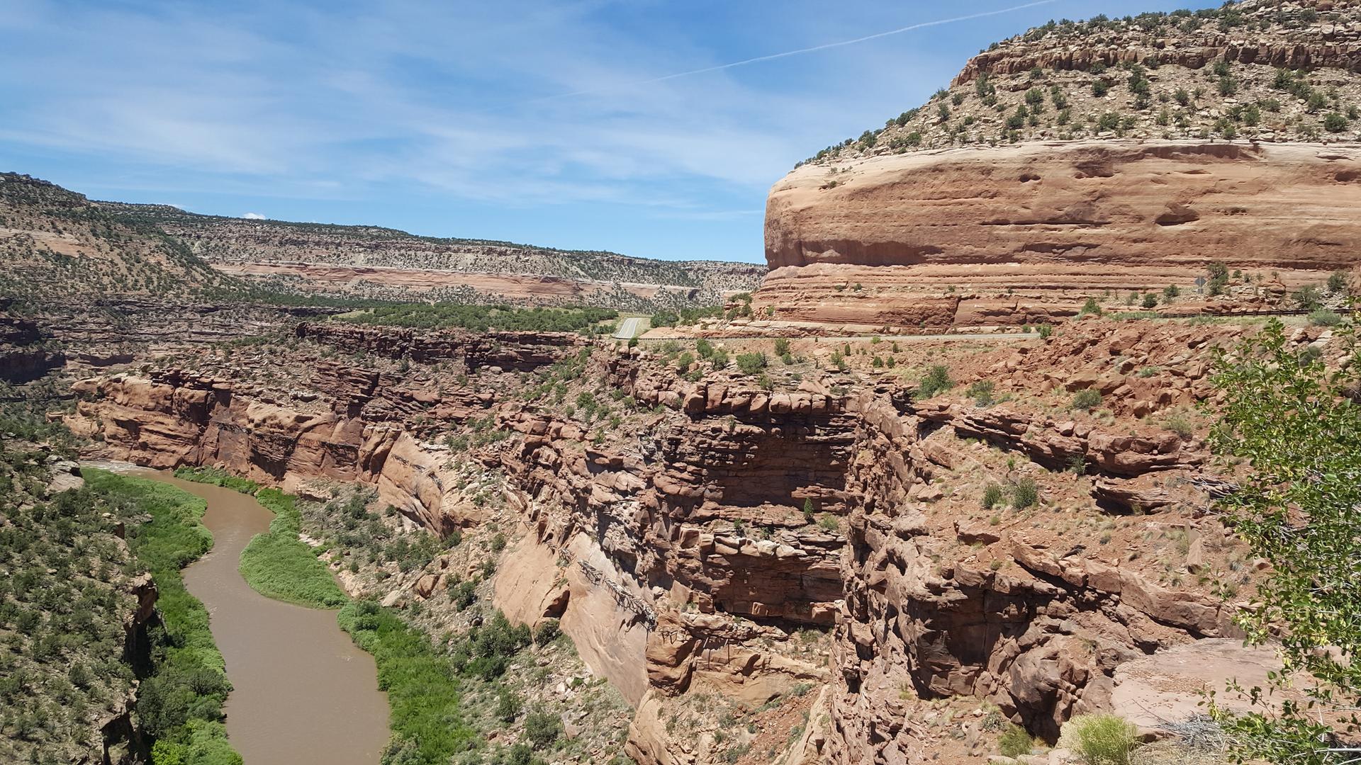 A wide, rocky canyon with a winding river under a bright blue sky.