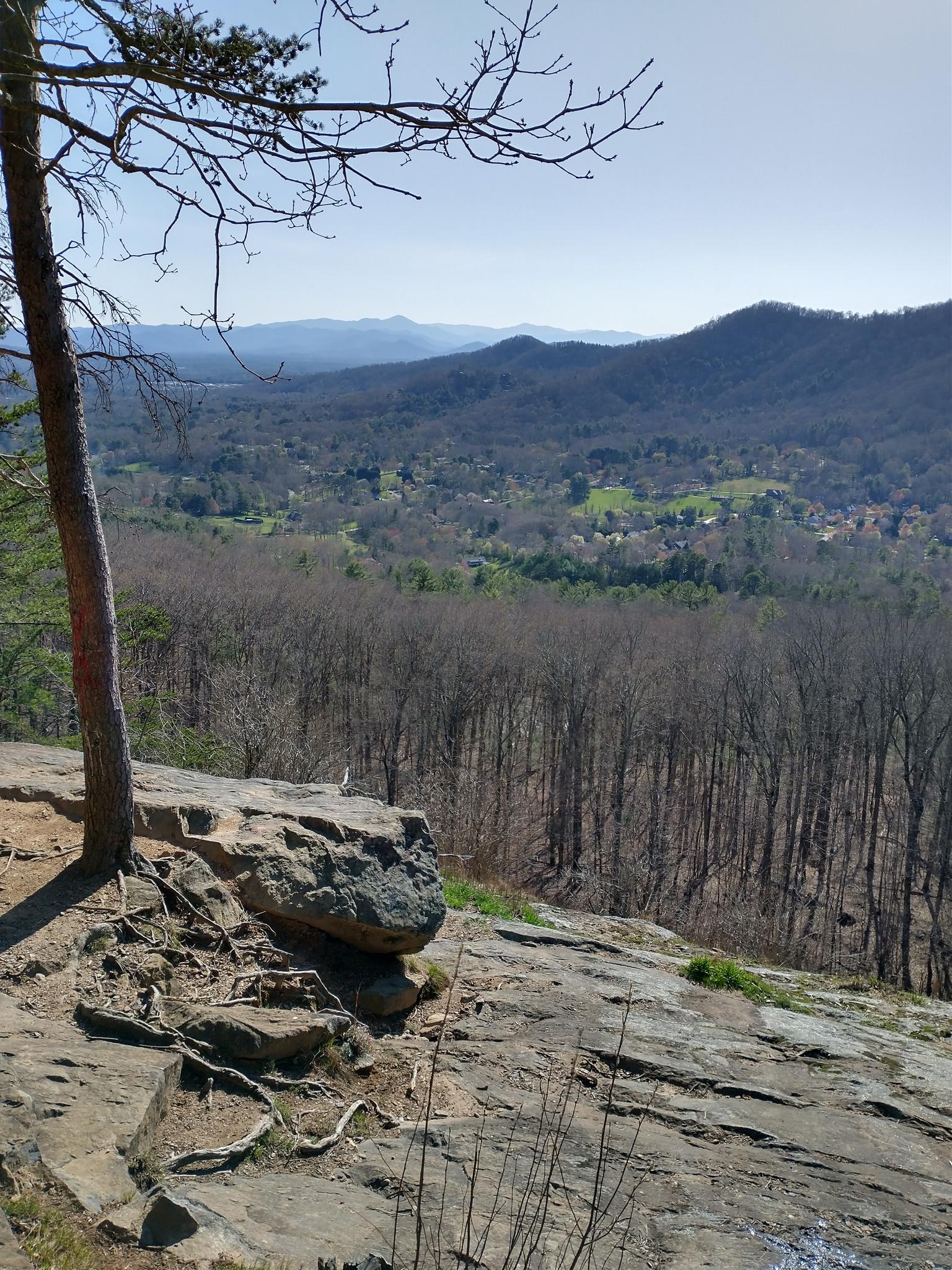 Sunny view from a rocky outcrop overlooking a valley and distant mountains.