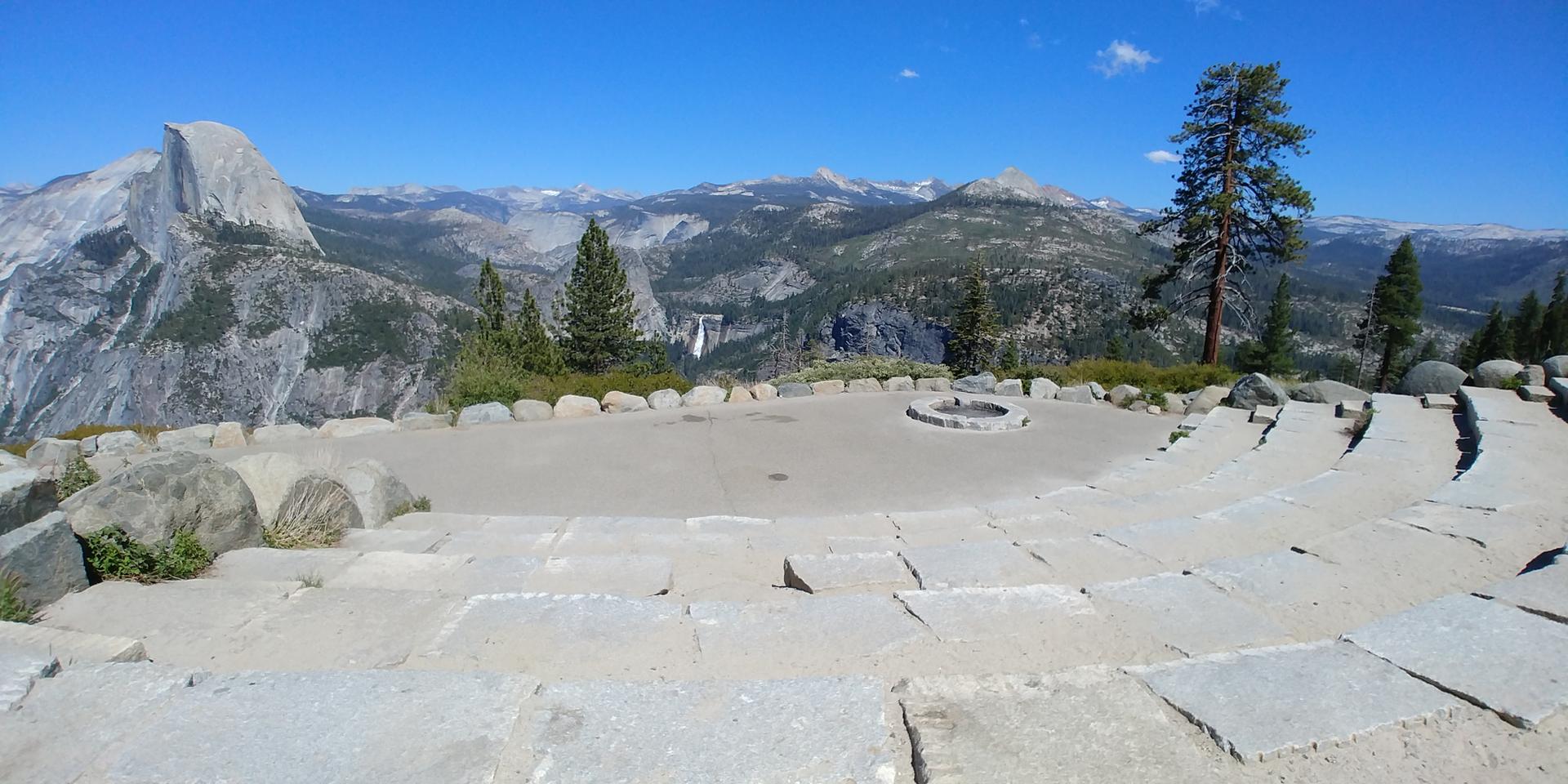 Stone amphitheater overlooking a mountain valley with a distant waterfall.