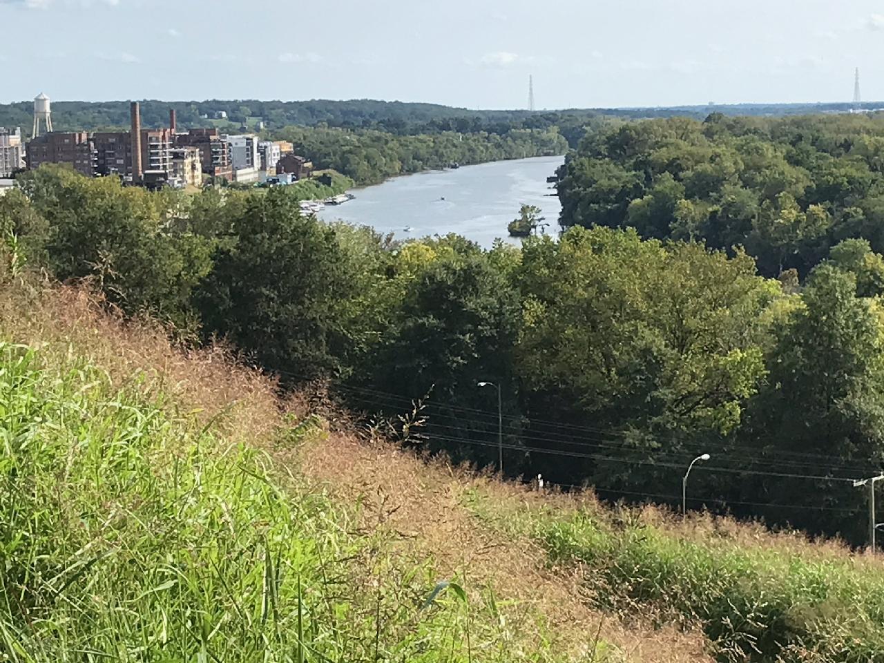 Grassy hillside overlooking a winding river, distant buildings, and green trees.