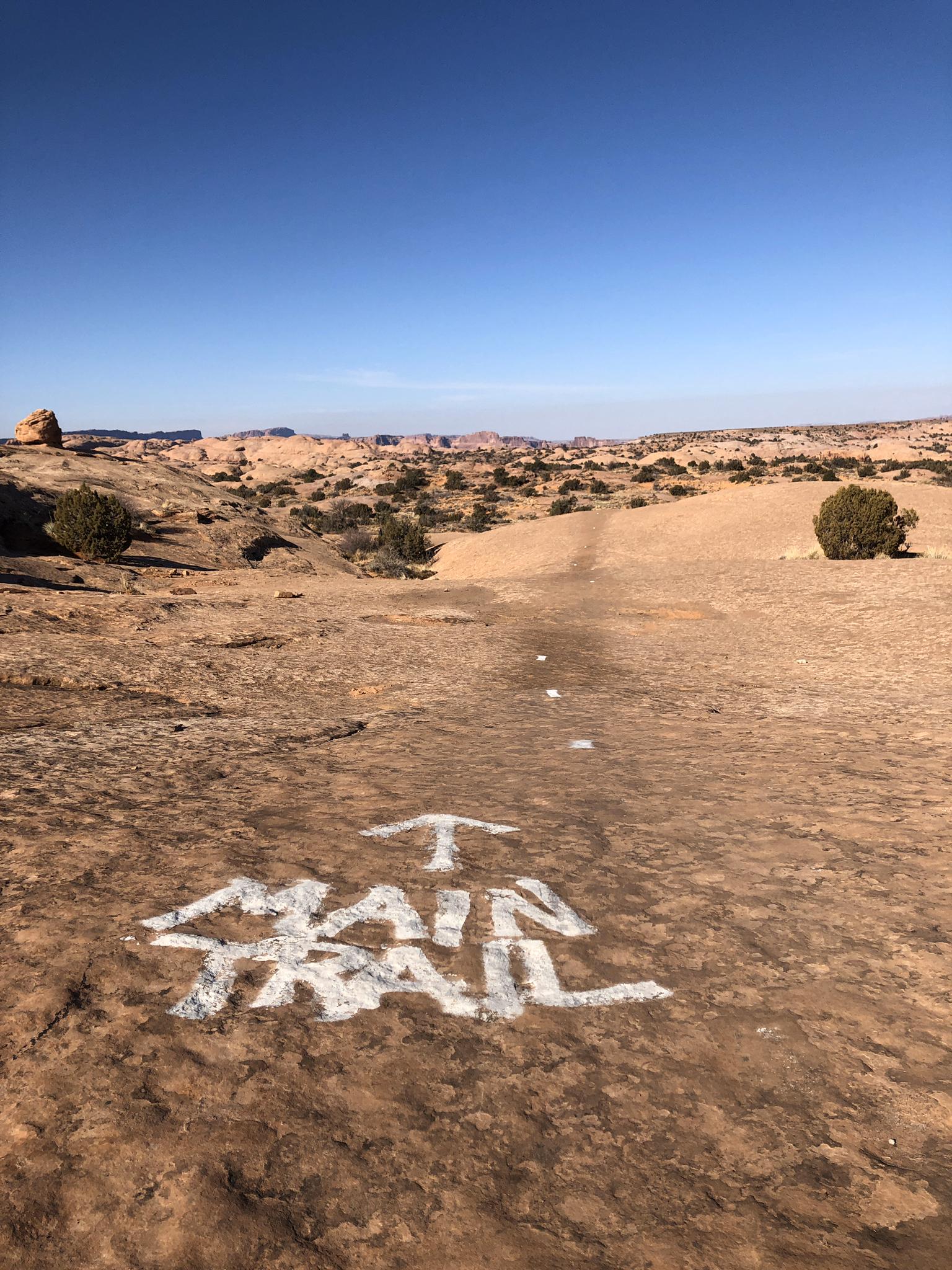 "Main Trail" painted on a flat rock surface in a sunny desert.