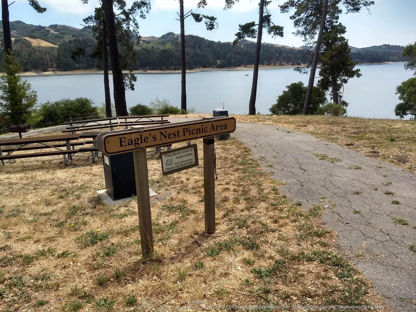 Picnic area sign and tables near a lake, surrounded by tall trees.