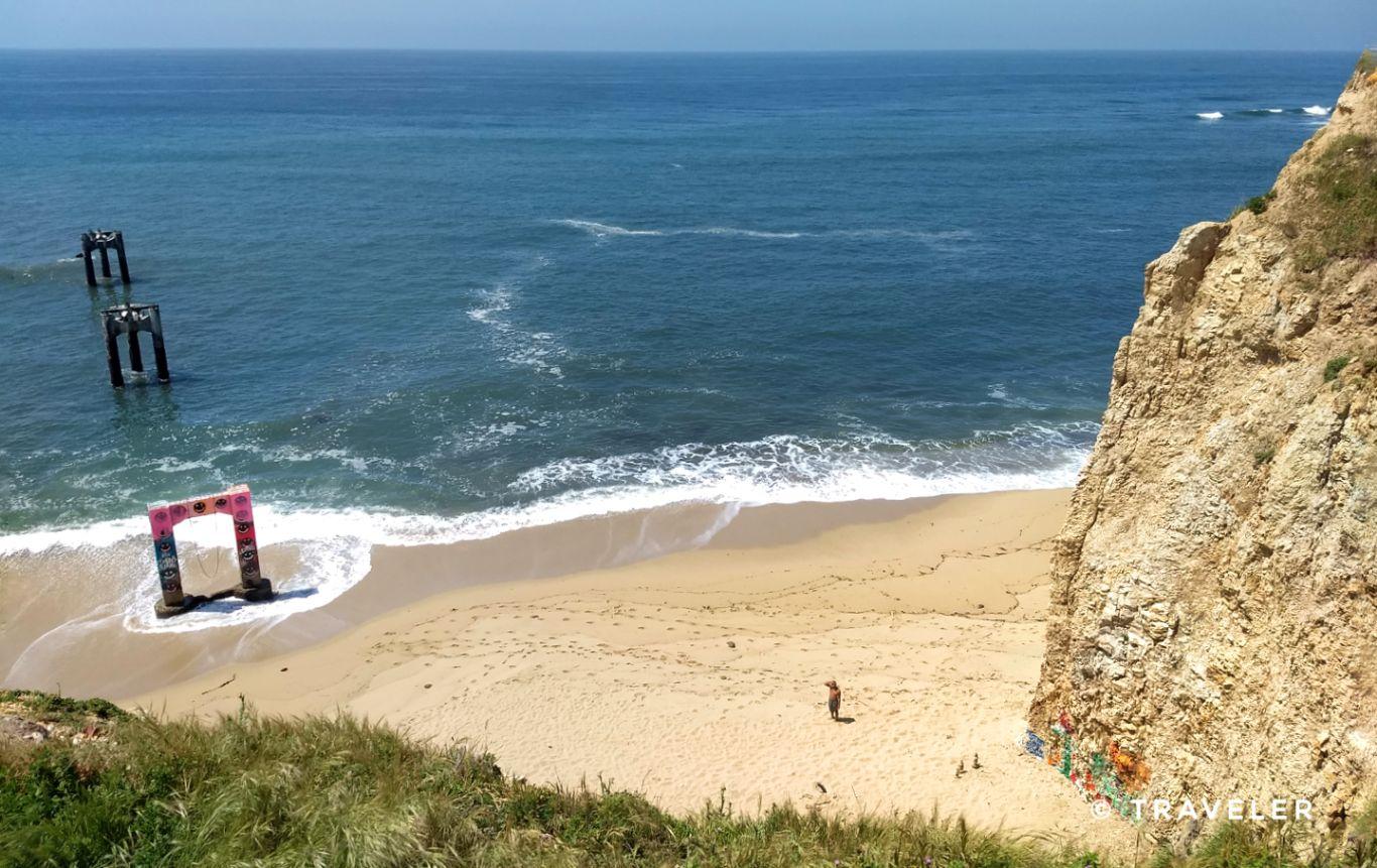 Sunny beach with ocean waves, concrete structures, and a distant person.