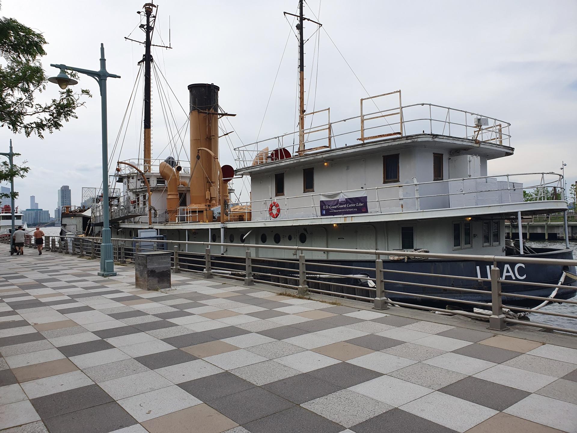 A large, old-fashioned boat docked at a pier with a city in background.