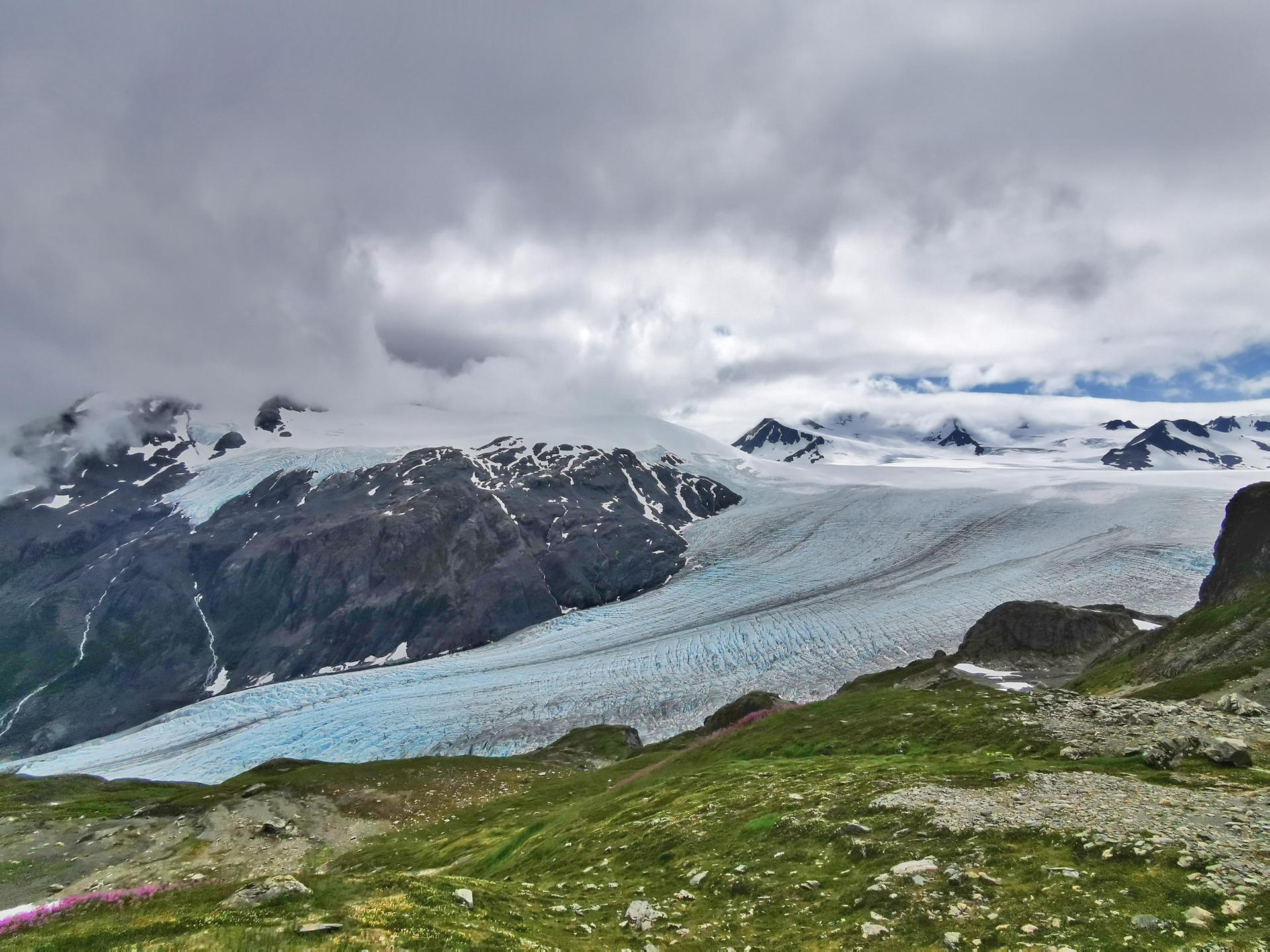 A wide glacier stretches across a mountain landscape under a cloudy sky.