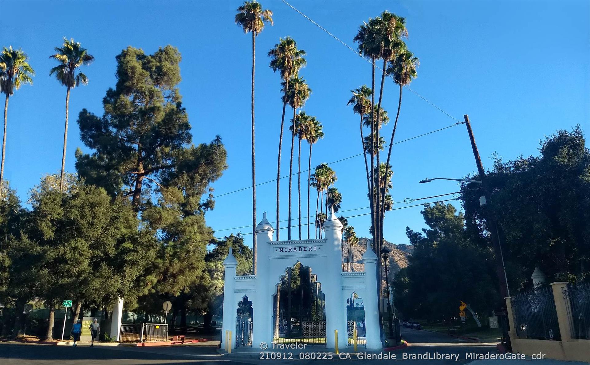 White archway gate under tall palm trees on a bright day.
