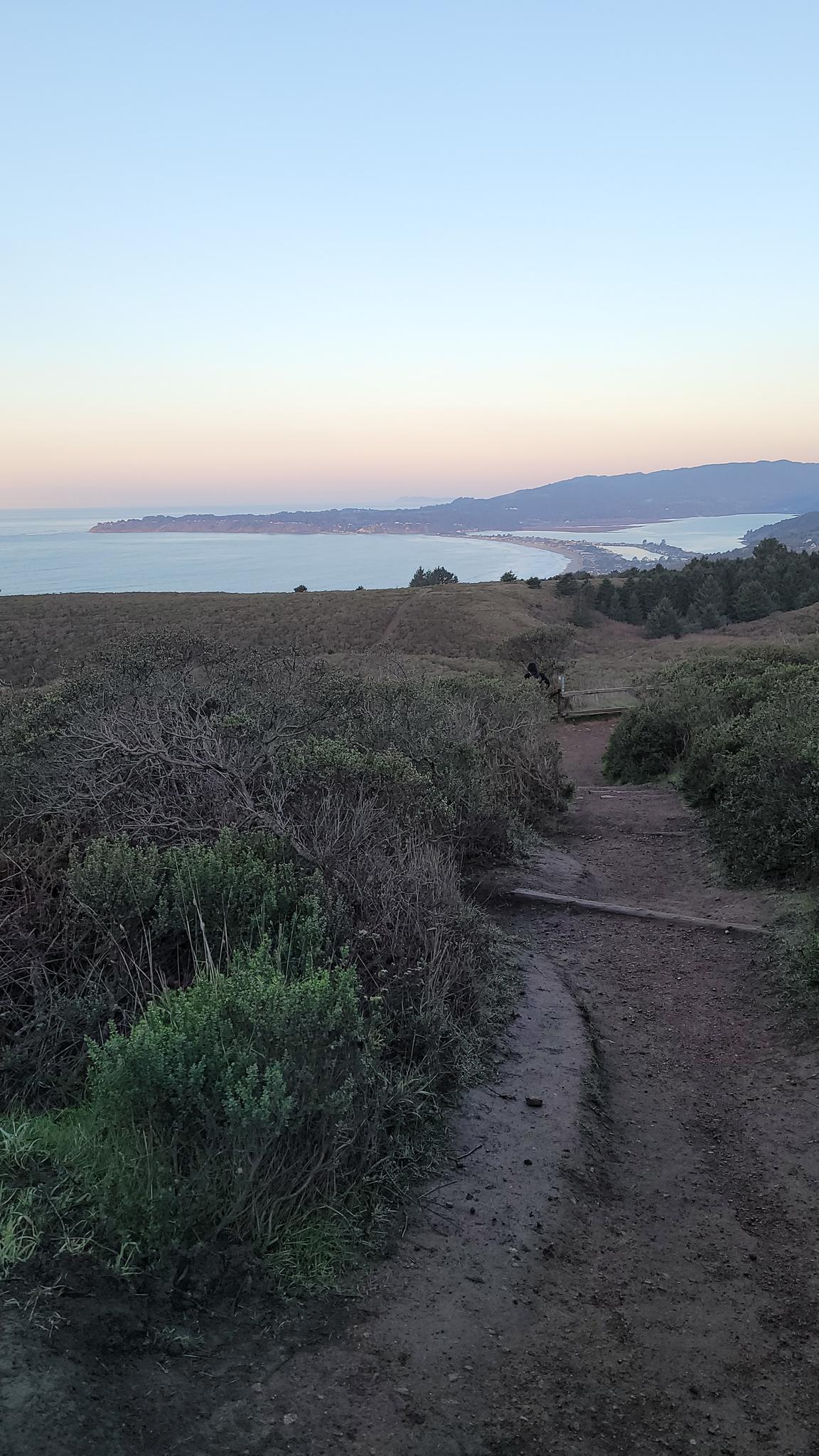 Dirt path leading to a vast ocean view at dusk.