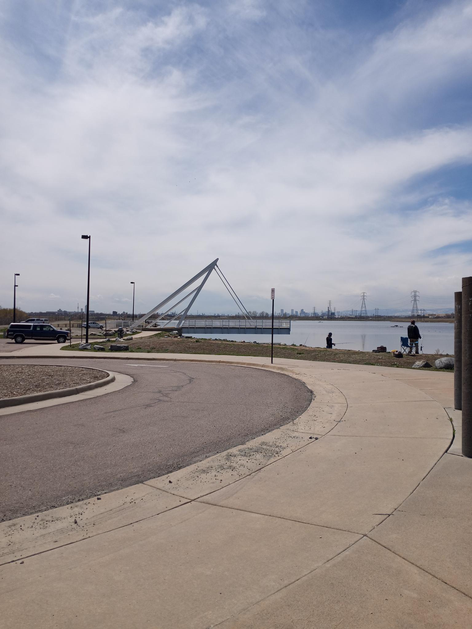 Paved path curving towards a lake with a modern bridge and people.