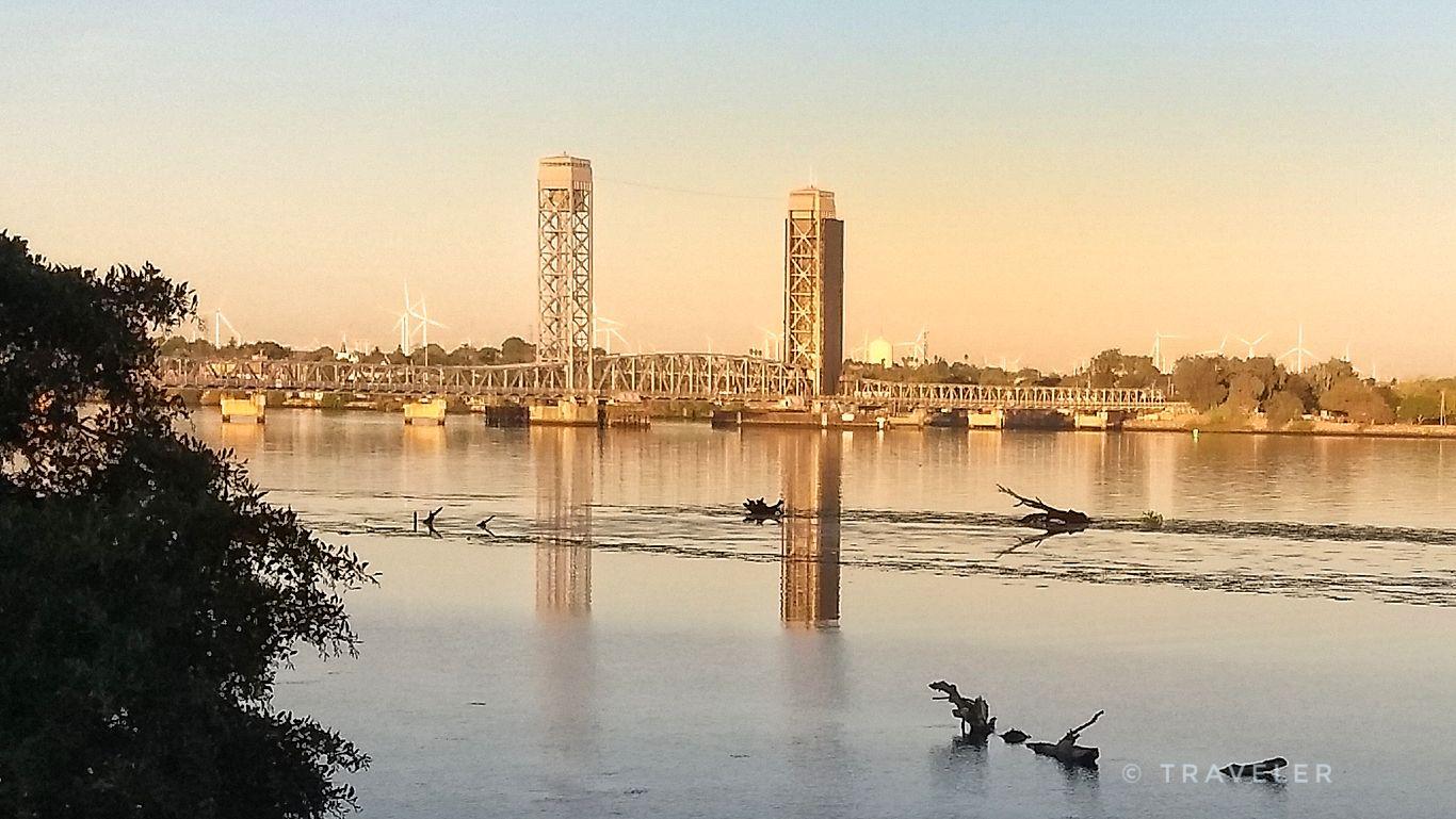 Distant bridge with tall towers over a wide river at golden hour.