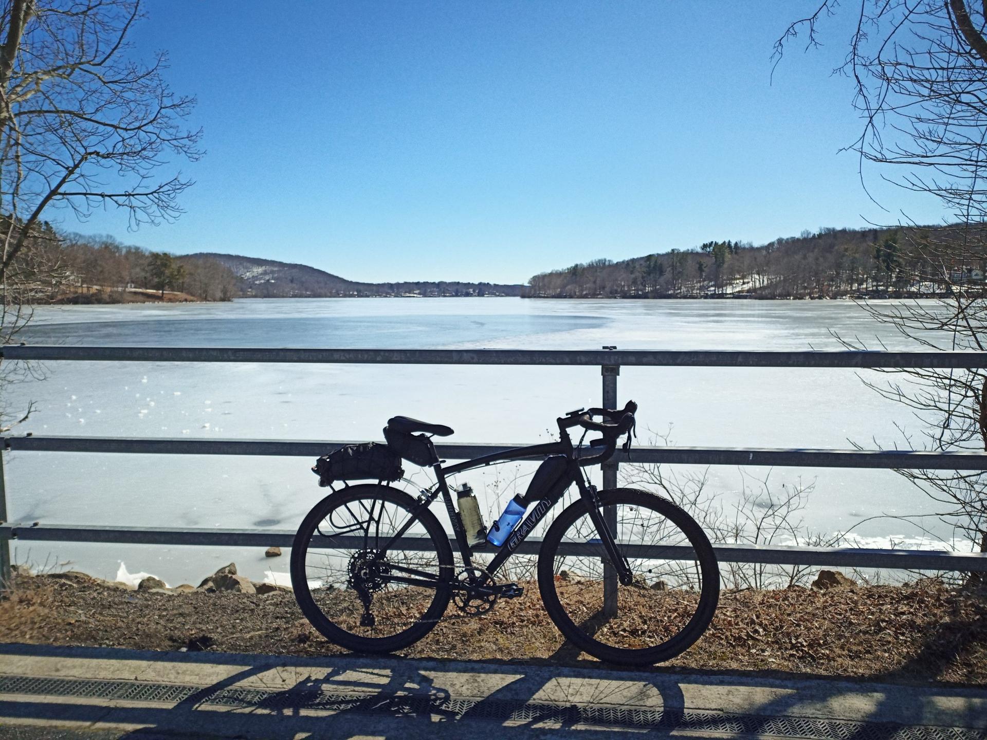 A bicycle parked by a railing overlooking a frozen lake under blue sky.