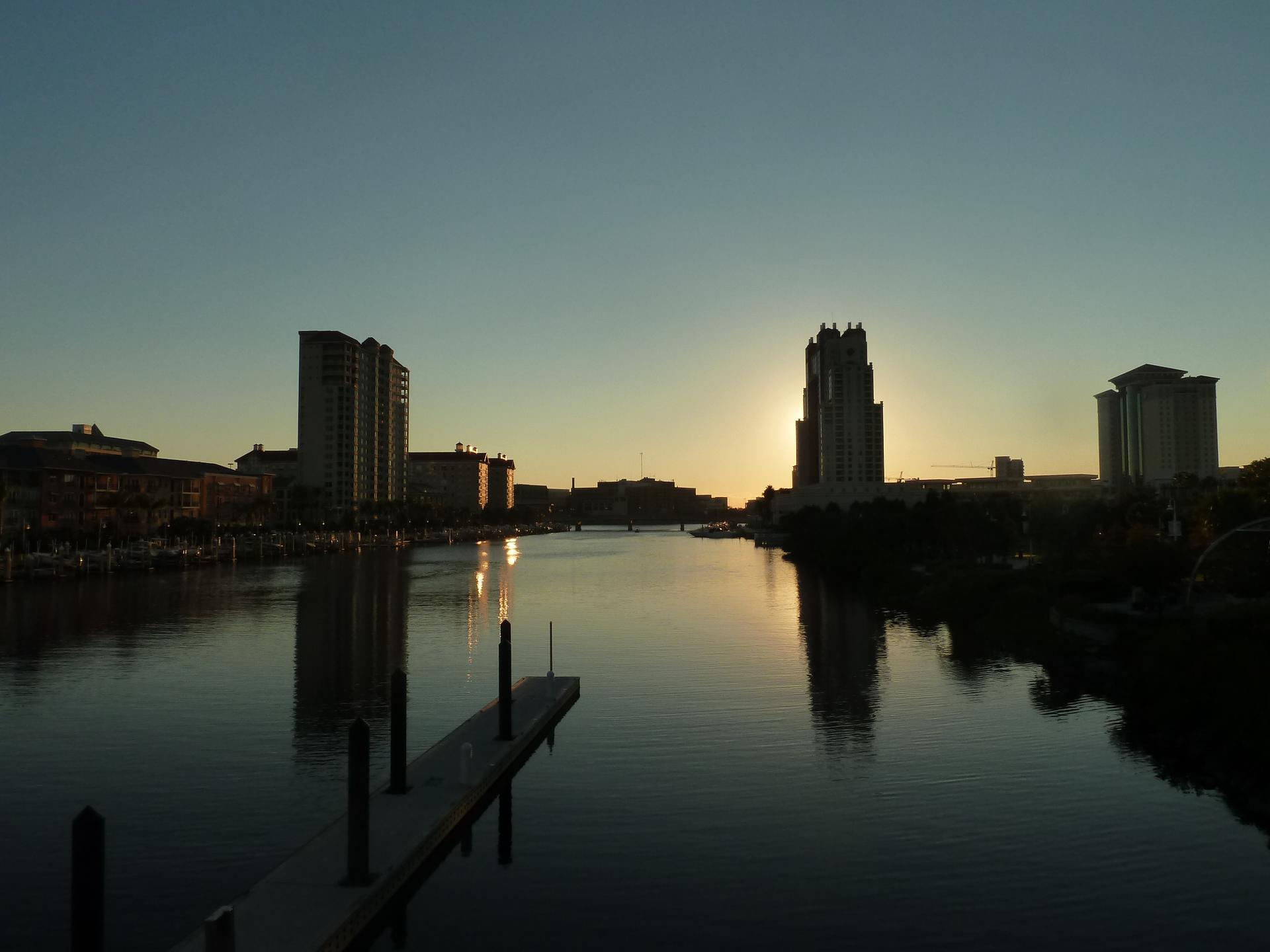 City skyline silhouetted against a vibrant sunset over a calm river.
