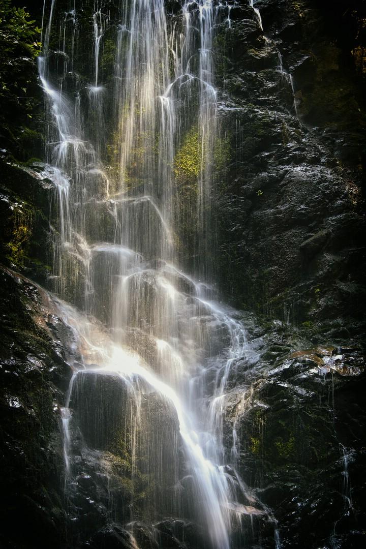 Close-up of a waterfall cascading over dark, mossy rocks.