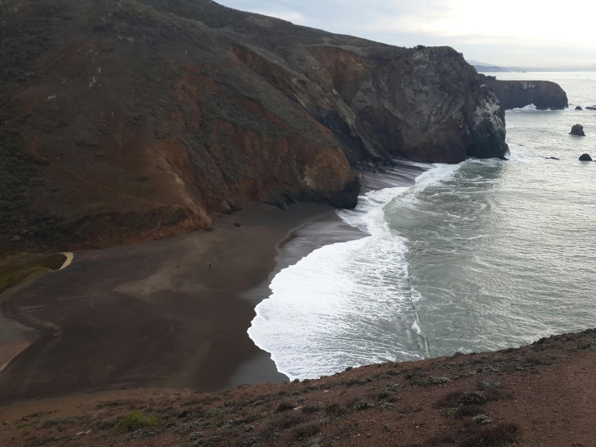 Dark sand beach with white waves crashing against steep cliffs.