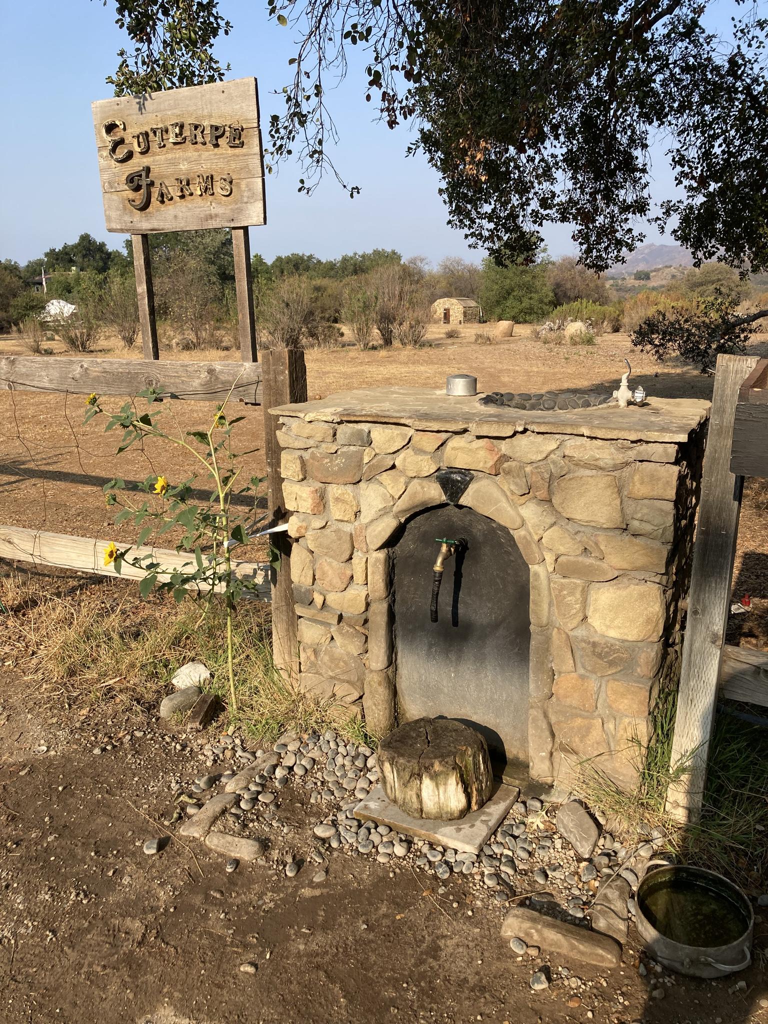 Stone water spigot and wooden sign in a dry, sunny rural landscape.