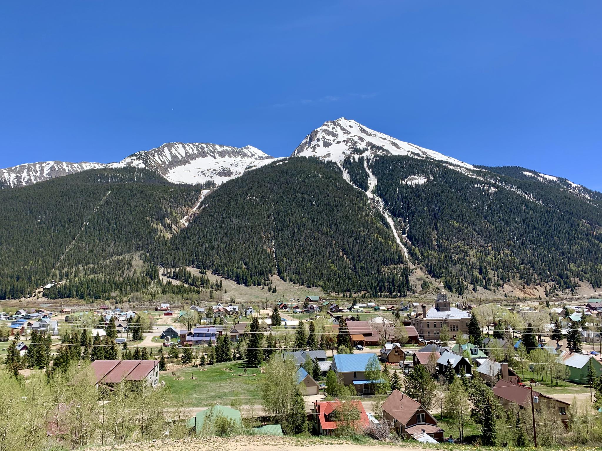 Sunny day over a town nestled in a valley with large, snow-capped mountains.
