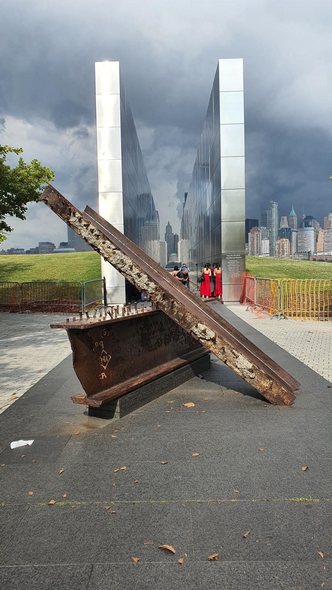 Metal sculpture with two tall reflective walls, people in background.
