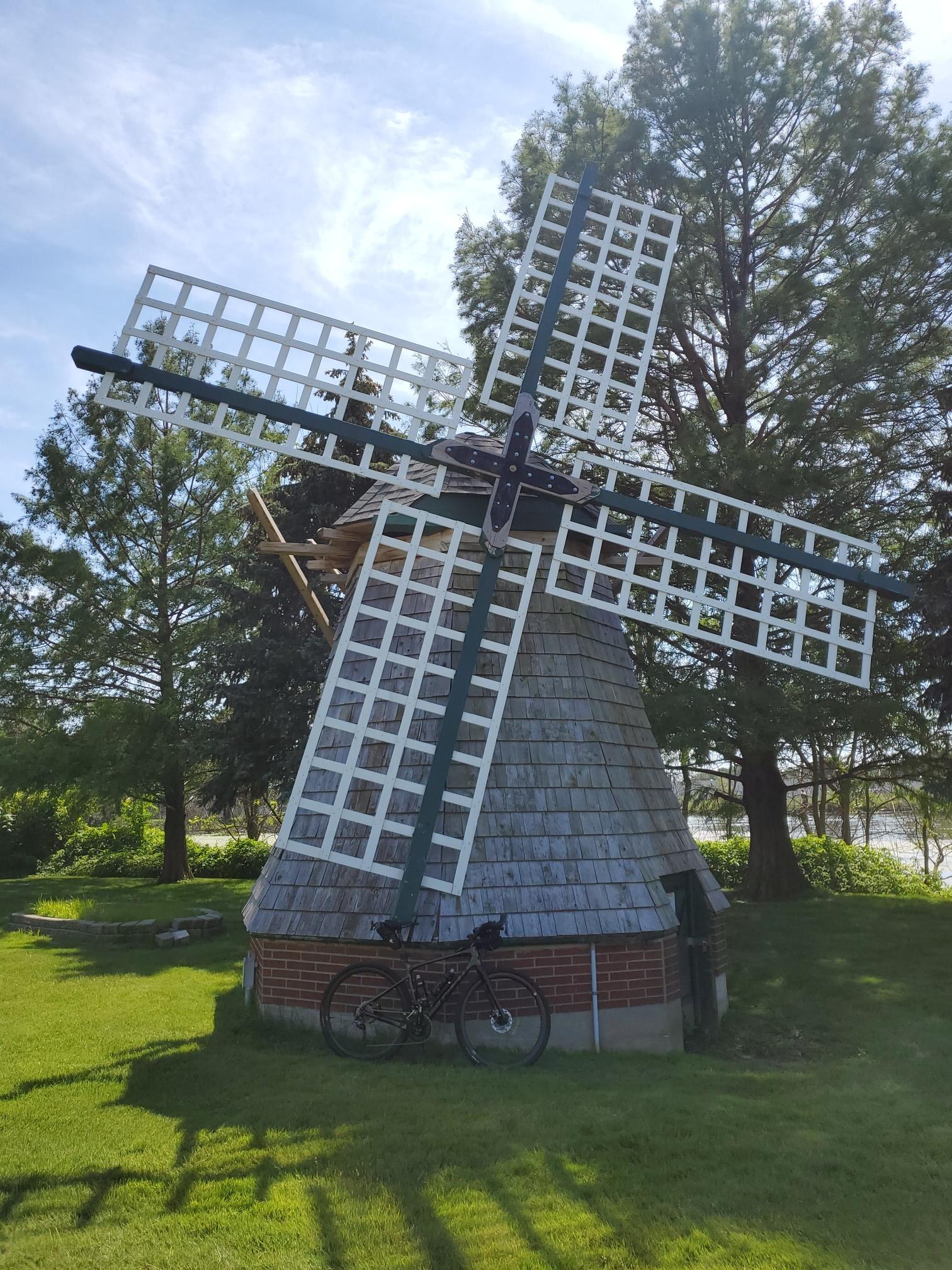 A traditional windmill with a bicycle parked on a sunny grassy lawn.