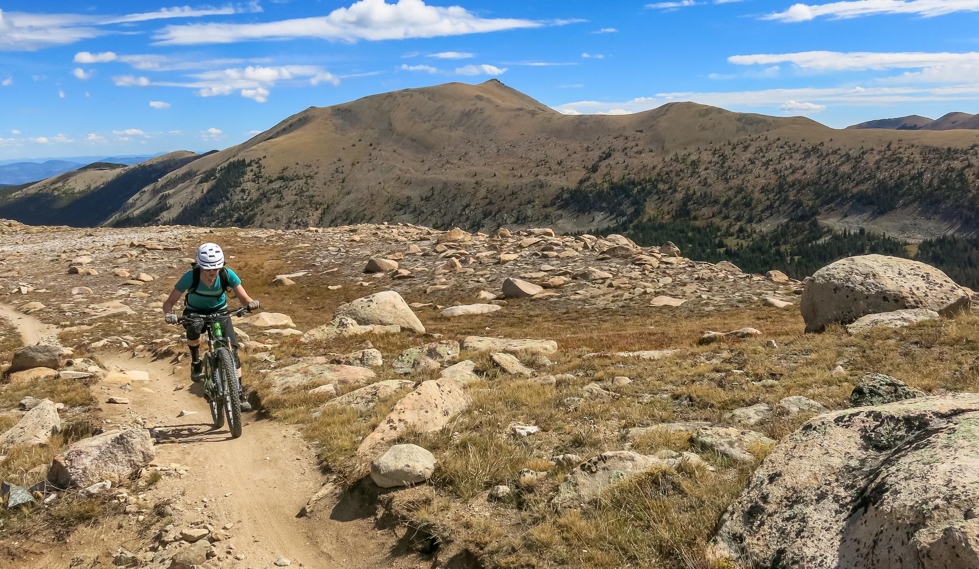 A person mountain biking on a rocky dirt trail under a bright, cloudy sky.
