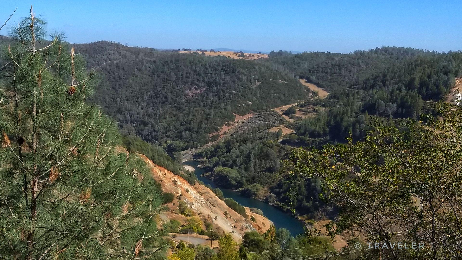 A winding river flows through a deep, sunlit, forested valley.