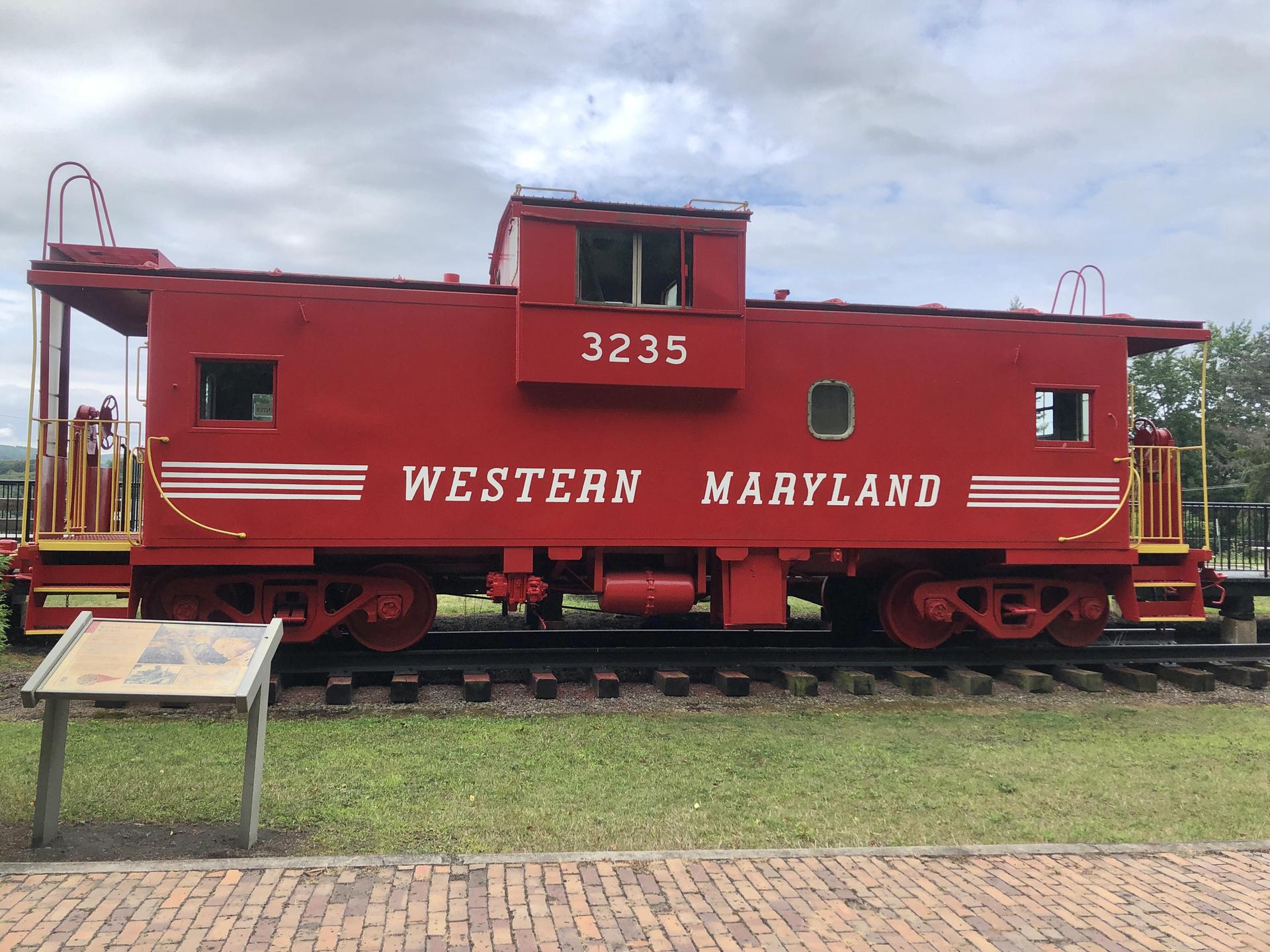 A bright red vintage train caboose sits on tracks under an overcast sky.