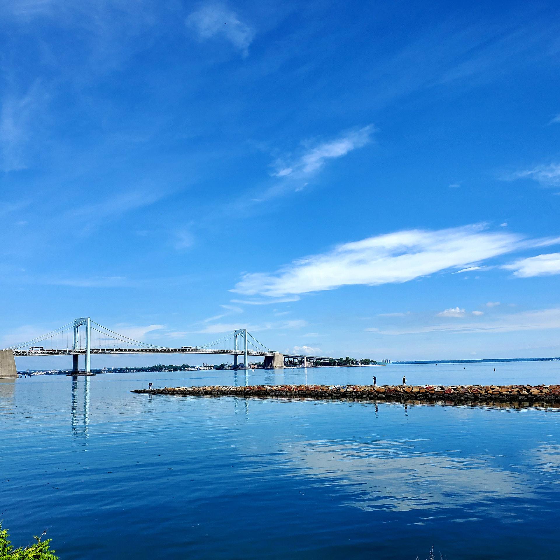 Vibrant blue sky over calm water, a bridge, and a distant rocky jetty.
