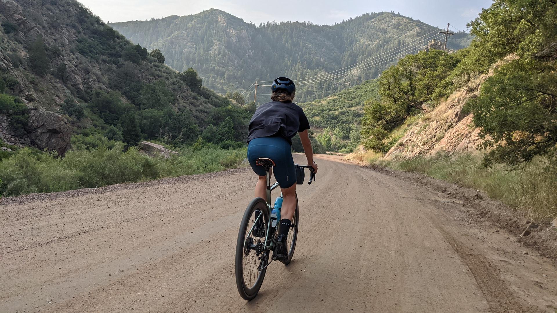 Cyclist on a dirt road in a mountain valley under an overcast sky.