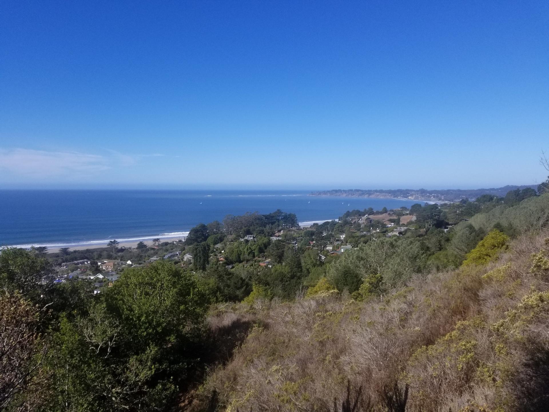 Panoramic view of a sunny coastline with ocean, beach, and distant town.