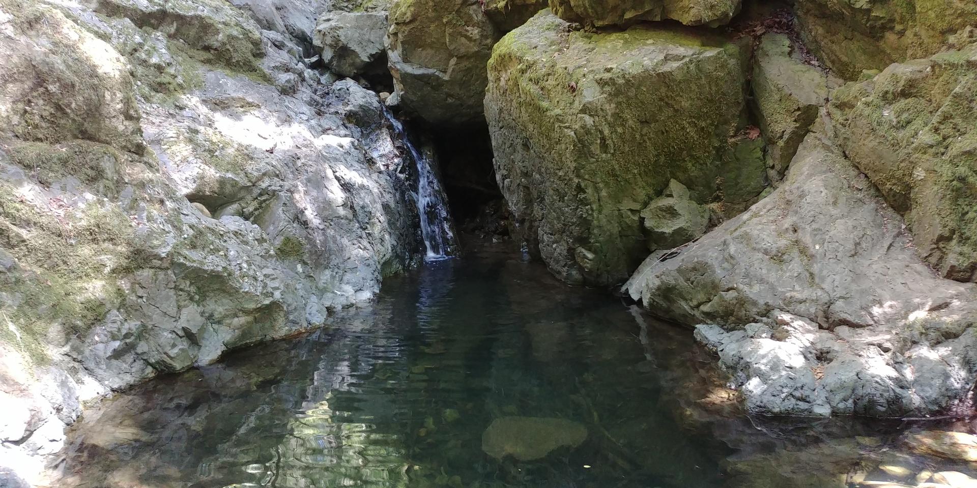Dark pool of water surrounded by large rocks, with a small waterfall.