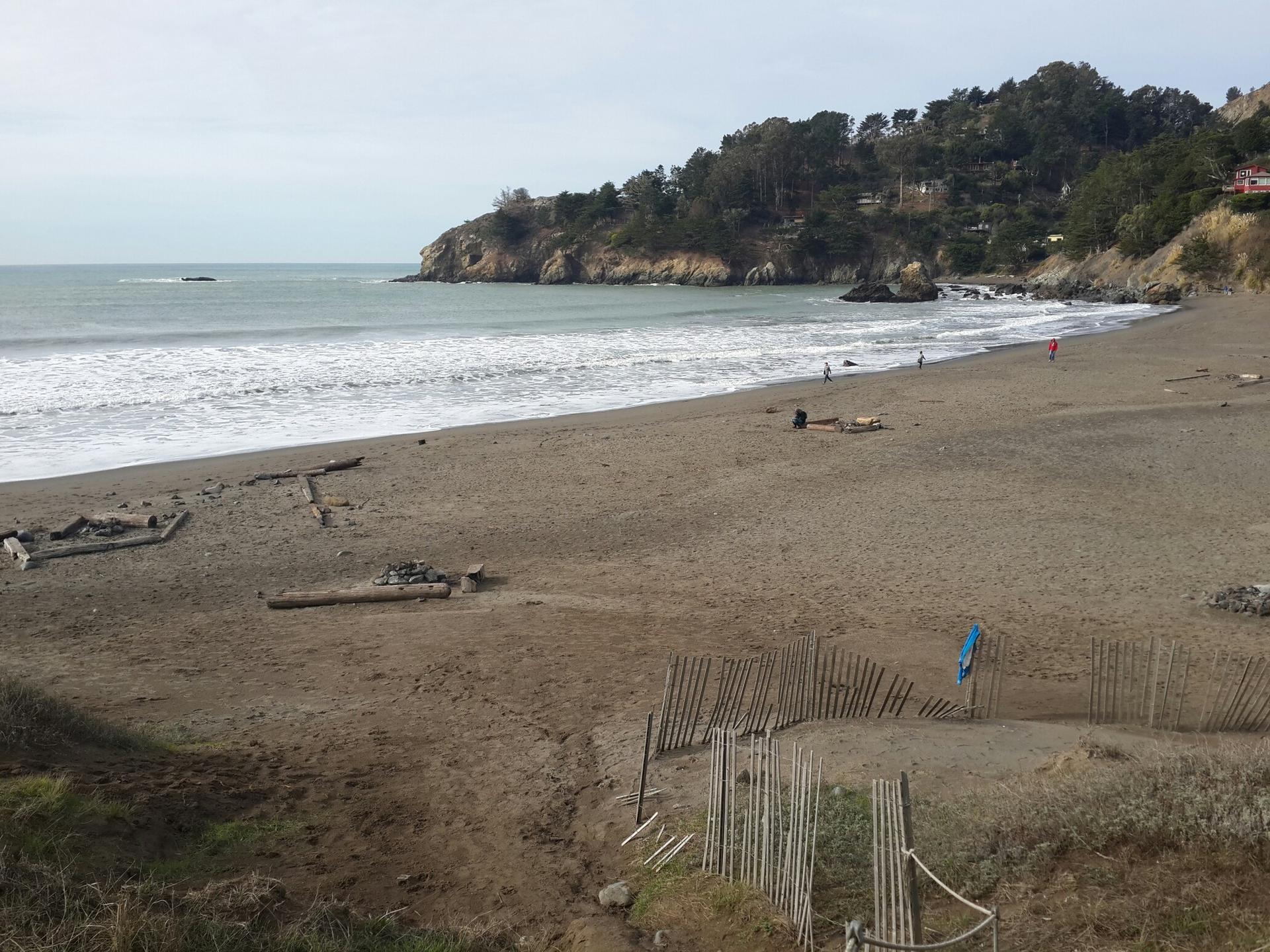 Cloudy day at a sandy beach with ocean waves and distant people.
