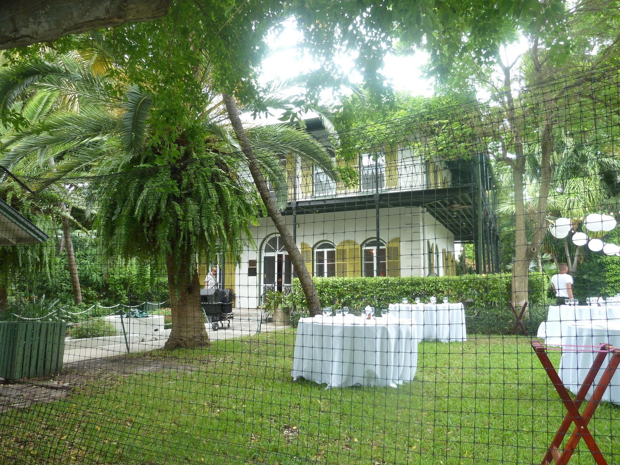 A grand house surrounded by lush tropical trees and outdoor event tables.