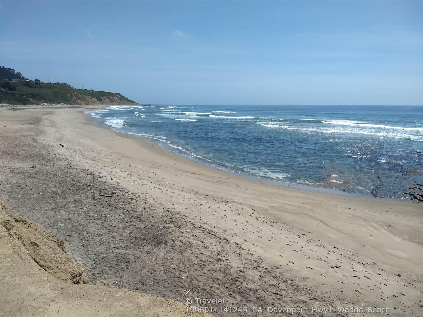 A wide sandy beach meets the ocean with waves under a clear sky.