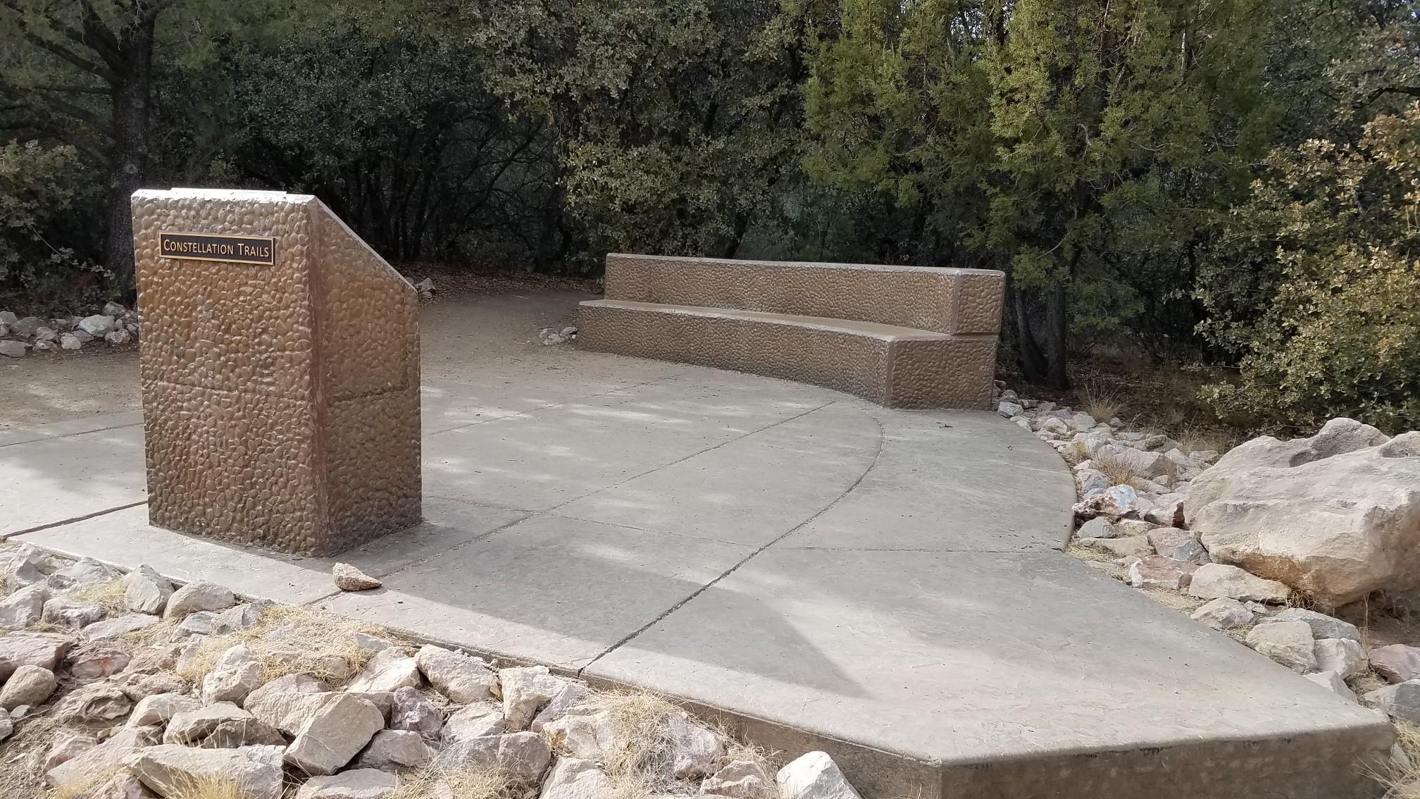 Concrete information kiosk and benches in a wooded area.